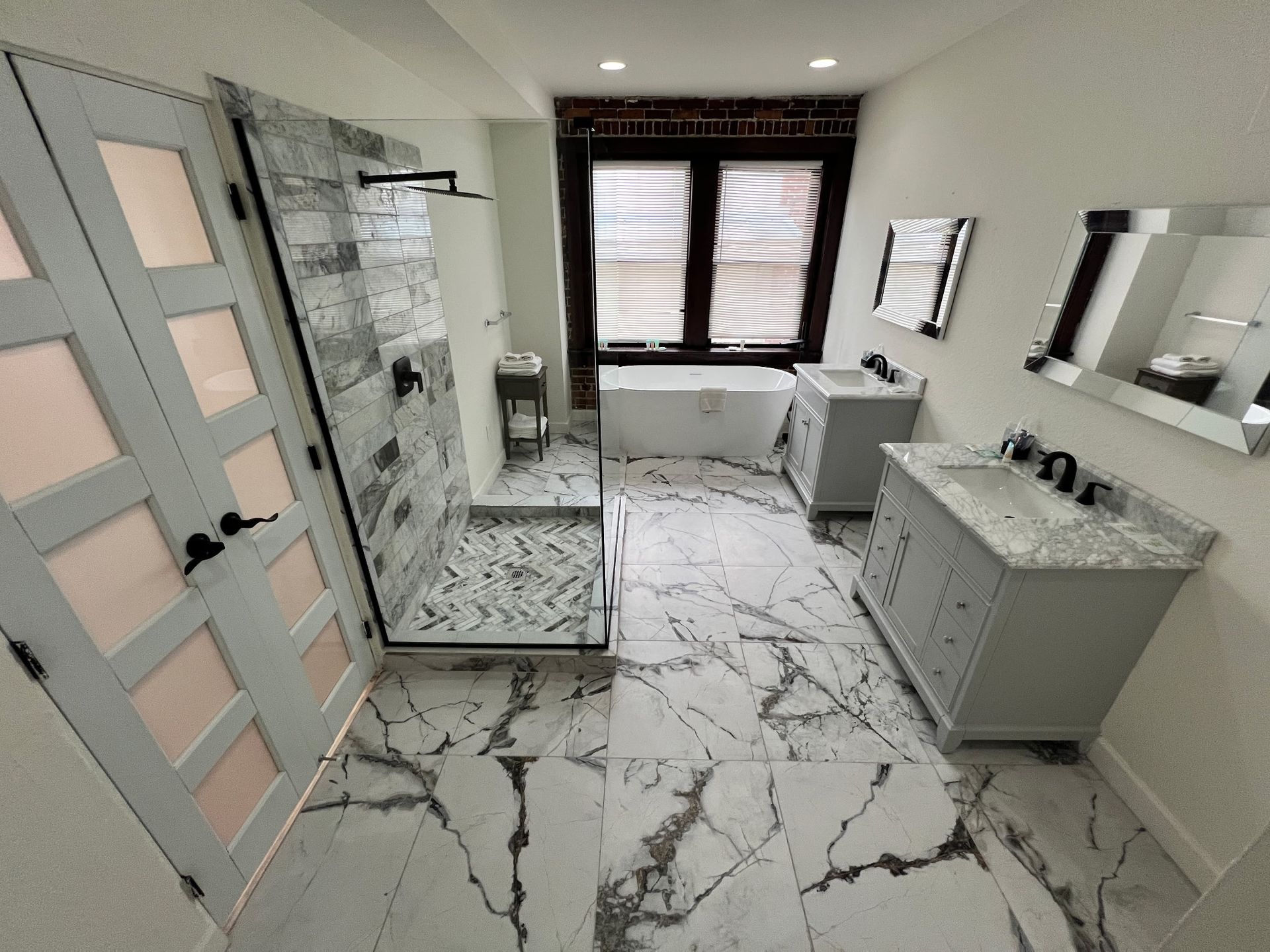 Modern bathroom with marble tile, glass shower, vanity, and window.