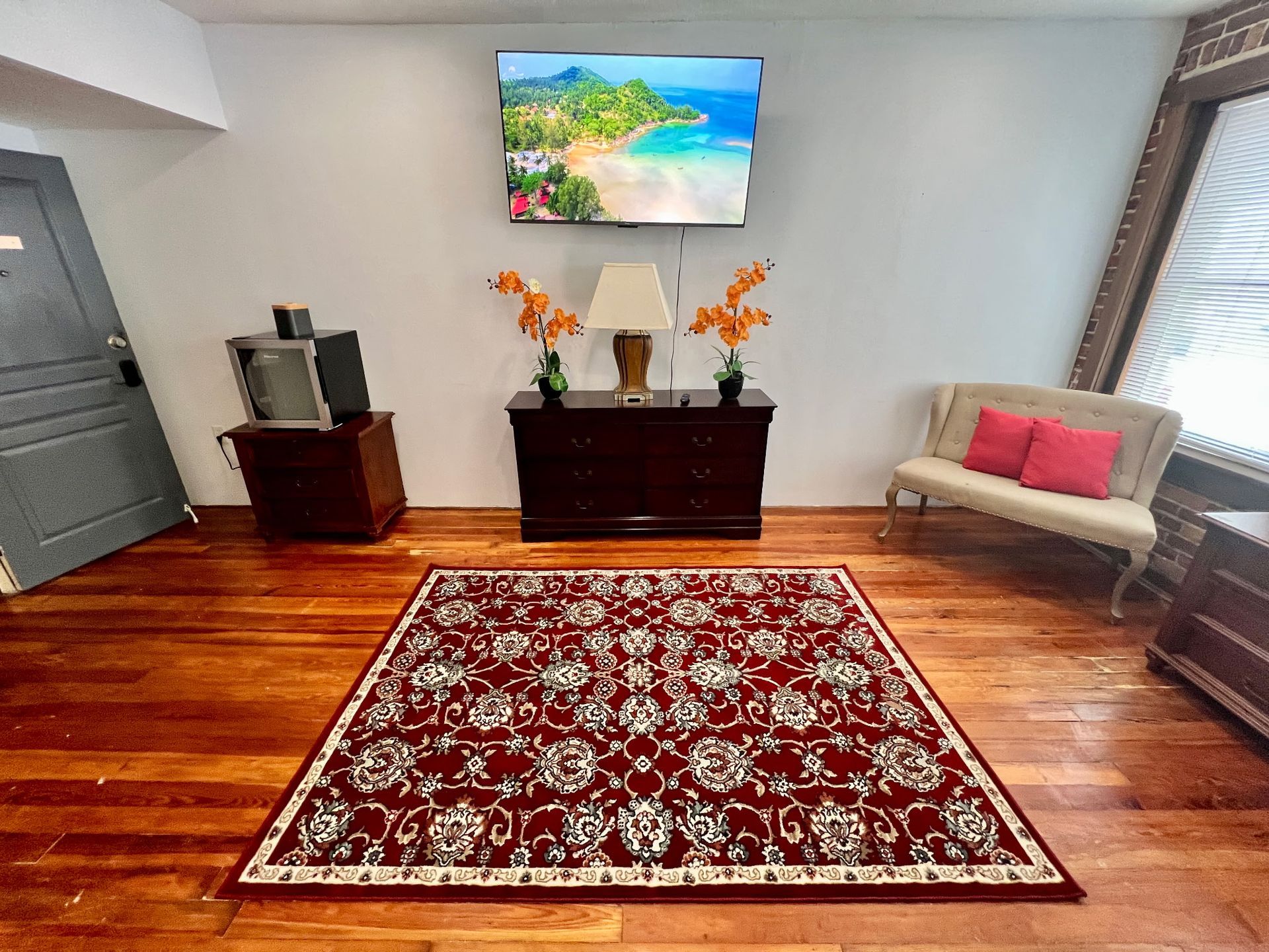 Bright living room with red patterned rug, wall art, sofa, cabinet, and hardwood floors