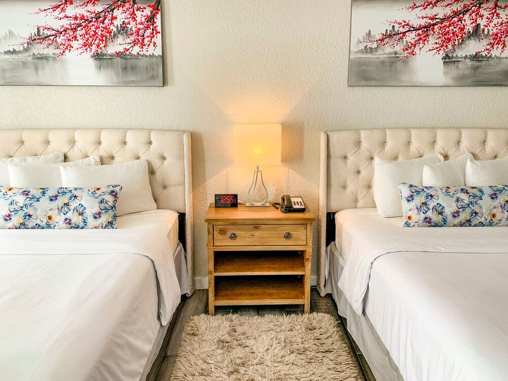 A bedroom with two beds , a nightstand , and two paintings on the wall.