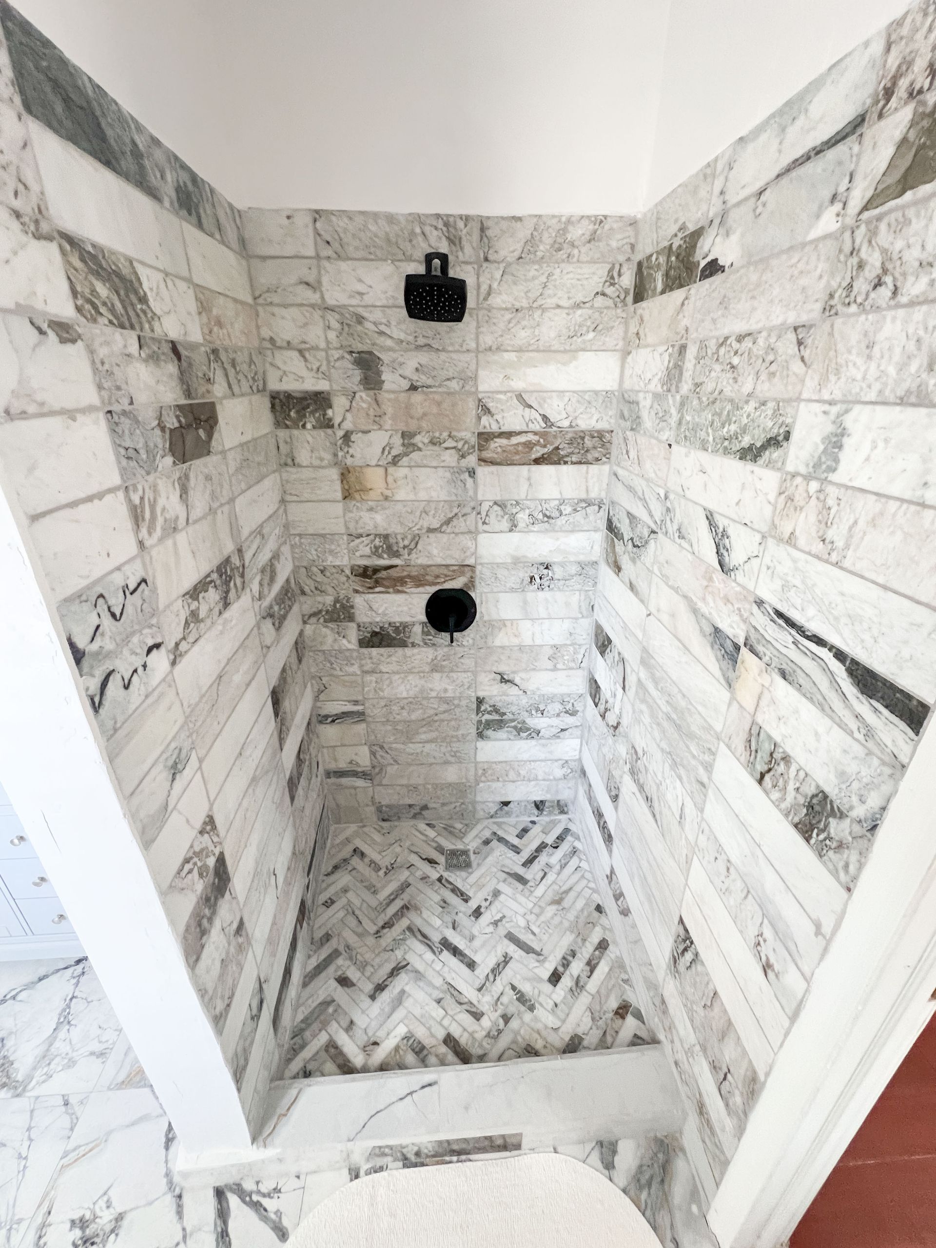Marble-tiled shower stall with herringbone floor and black shower fixtures