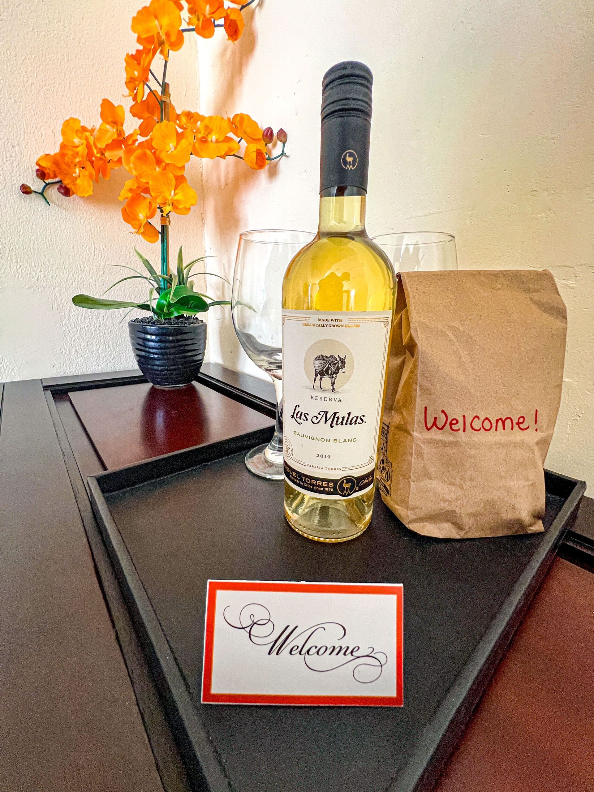 Welcome gift display with wine bottle, flowers, and brown paper bag on a tray