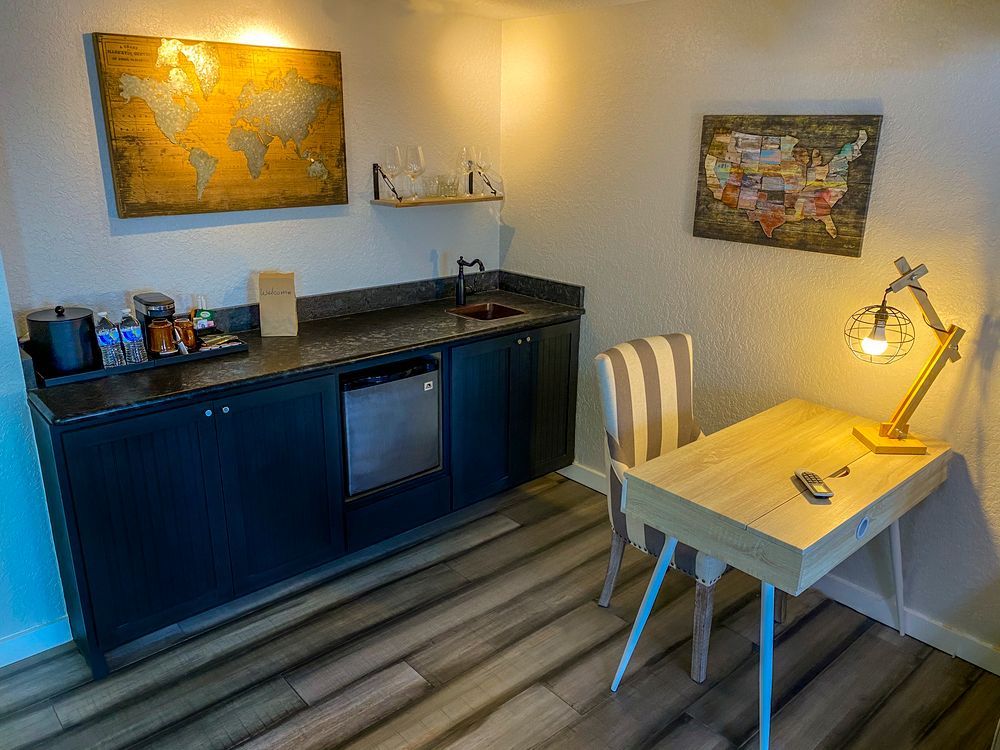 Small kitchenette with blue cabinets, table, chair, lamp, and wall art in a cozy room
