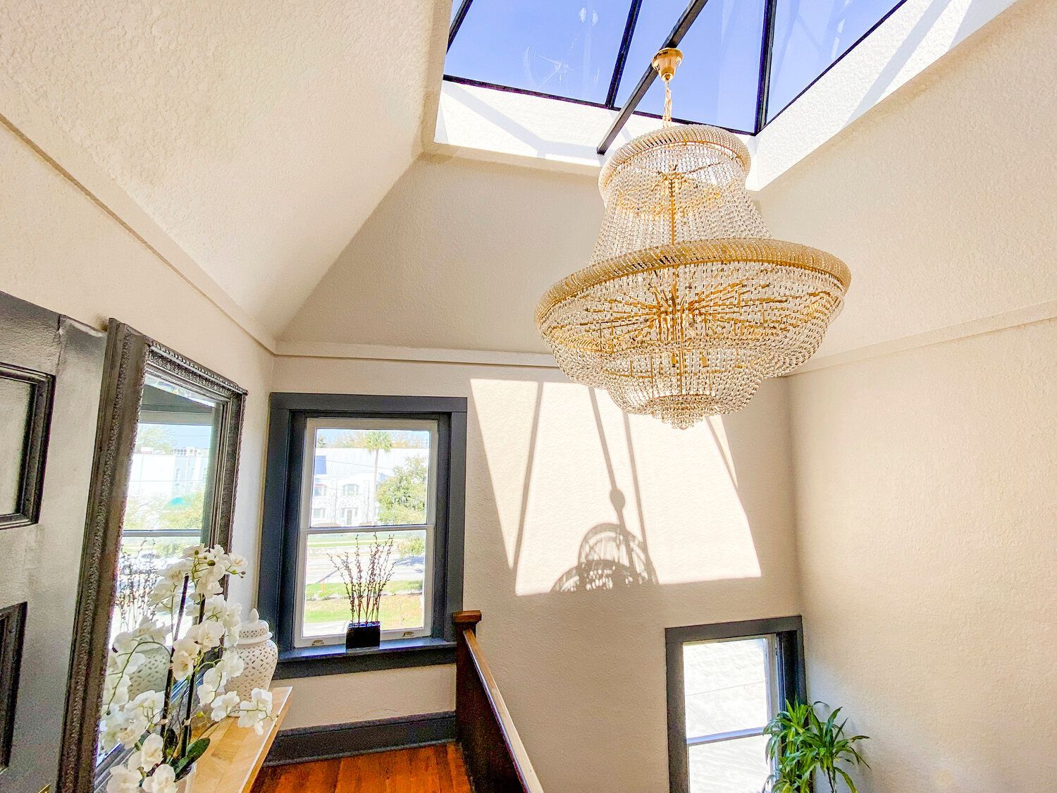 Bright hallway with a skylight, crystal chandelier, mirror, window, and potted plant