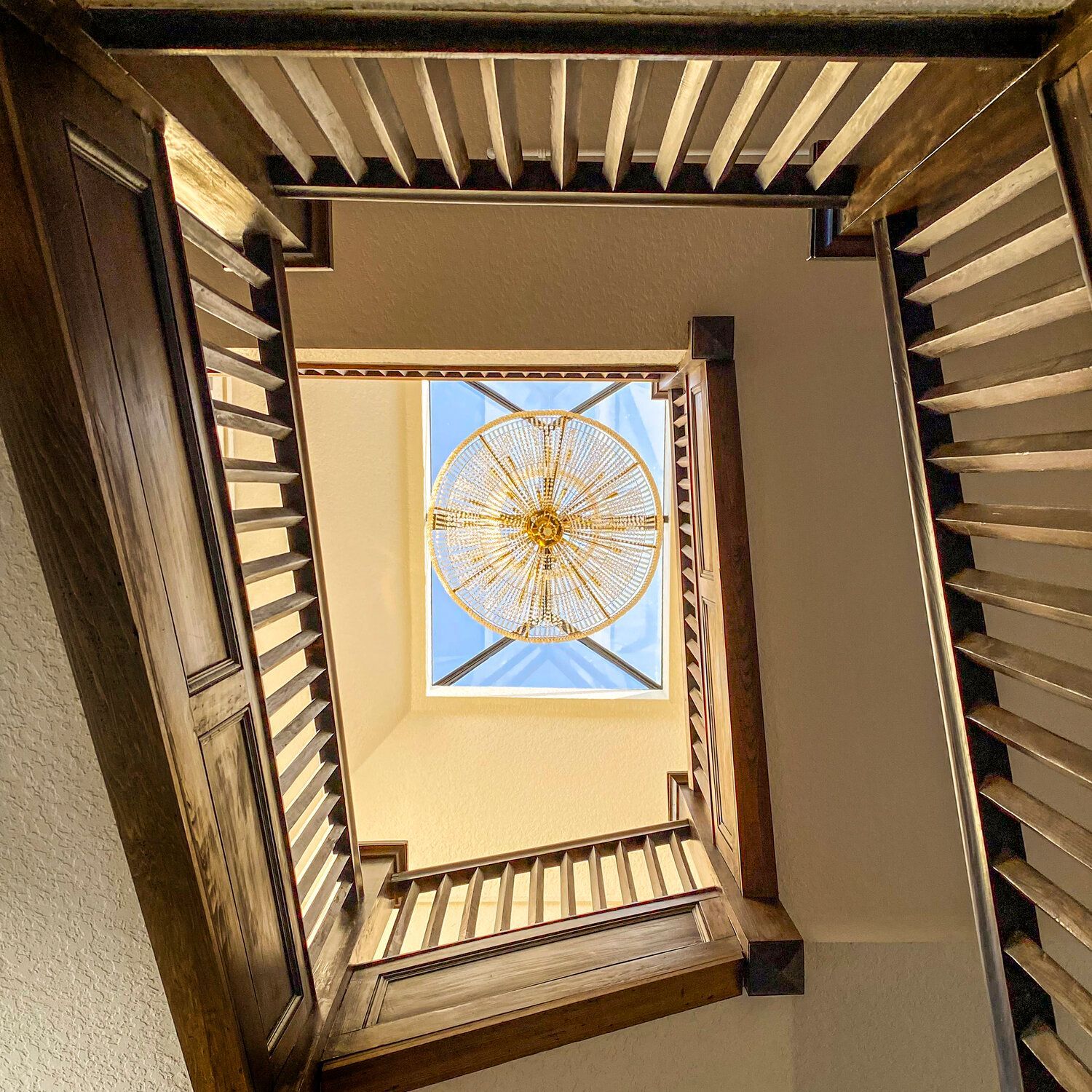 Looking up through a square skylight with a circular decorative pattern, framed by wooden stairwell railings.