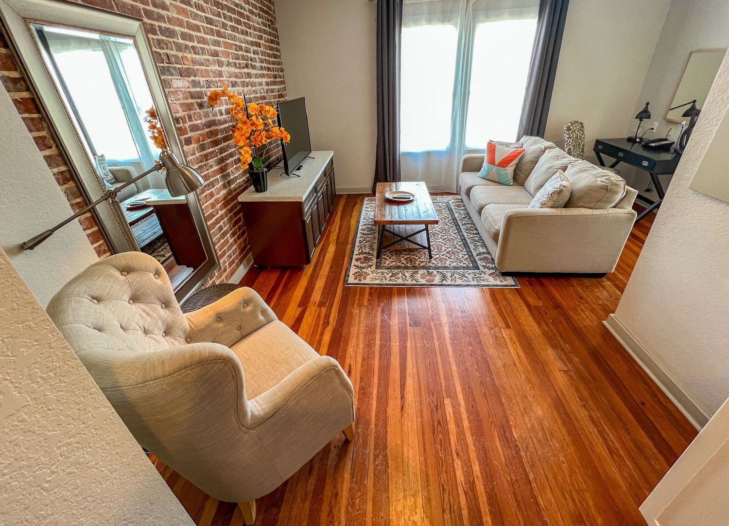 Bright living room with gray sofa, beige armchair, wooden floors, and a window by the balcony doors