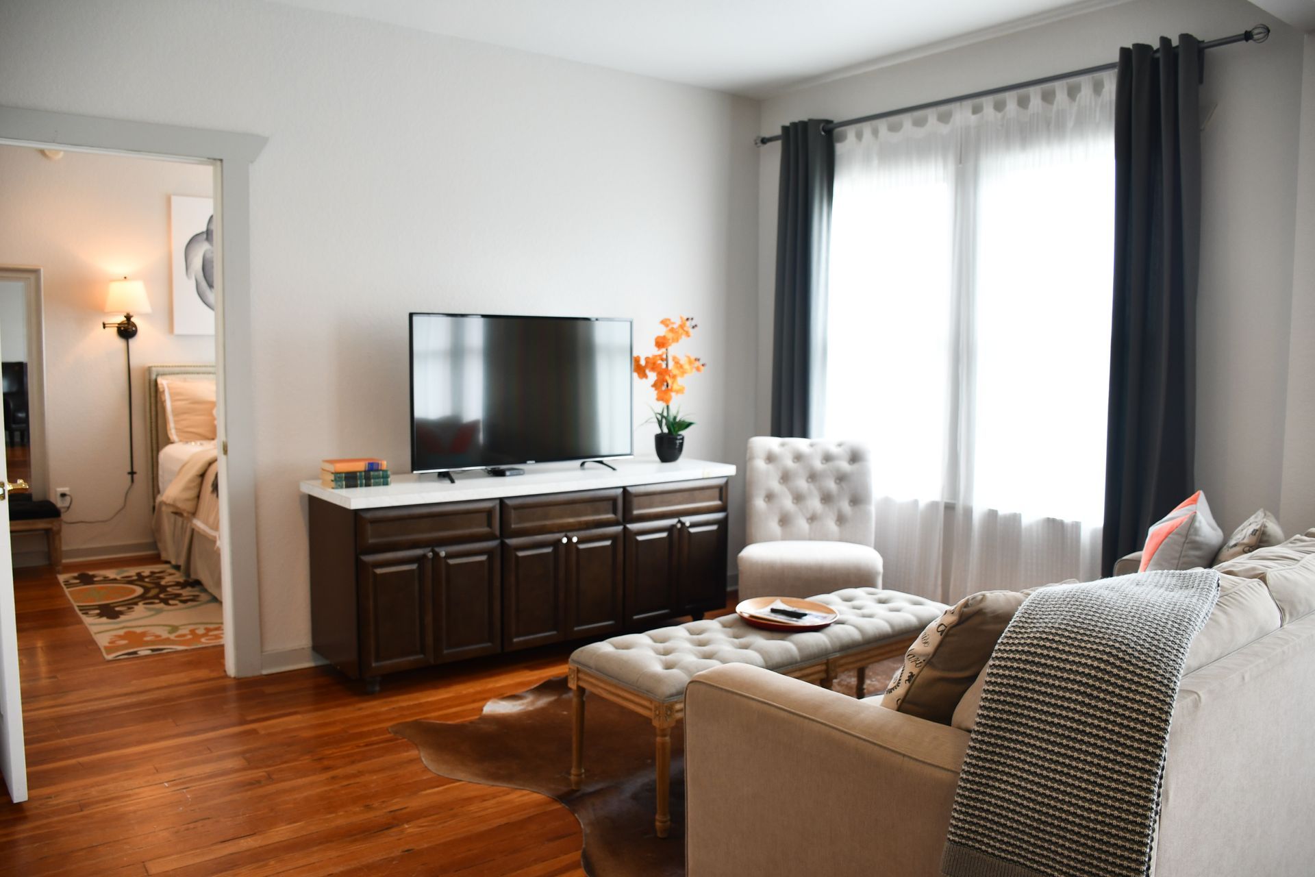 Cozy living room with sofa, TV on cabinet, armchair, and bright window with dark curtains