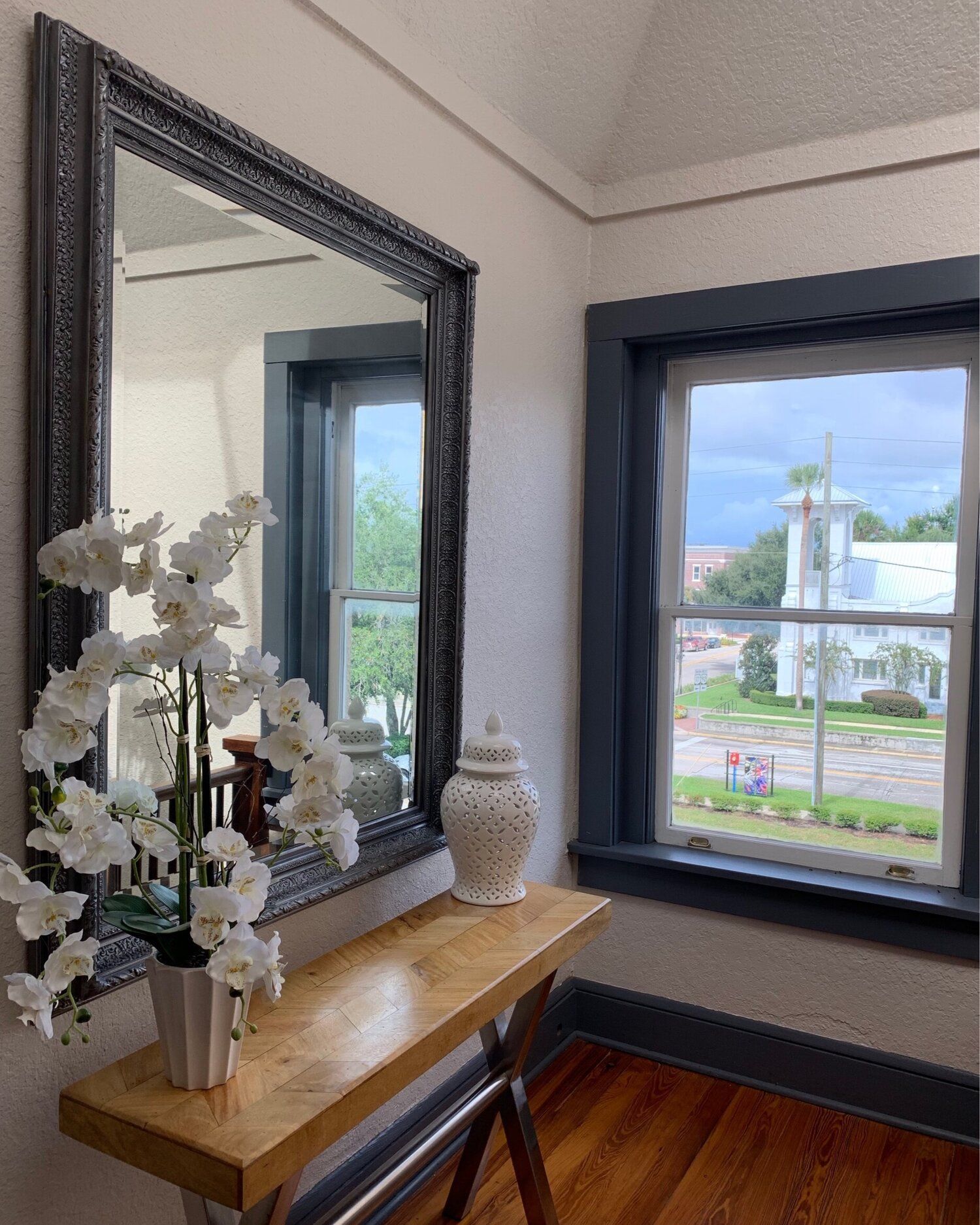 A decorated table beside a large mirror and window overlooking a street and fountain.
