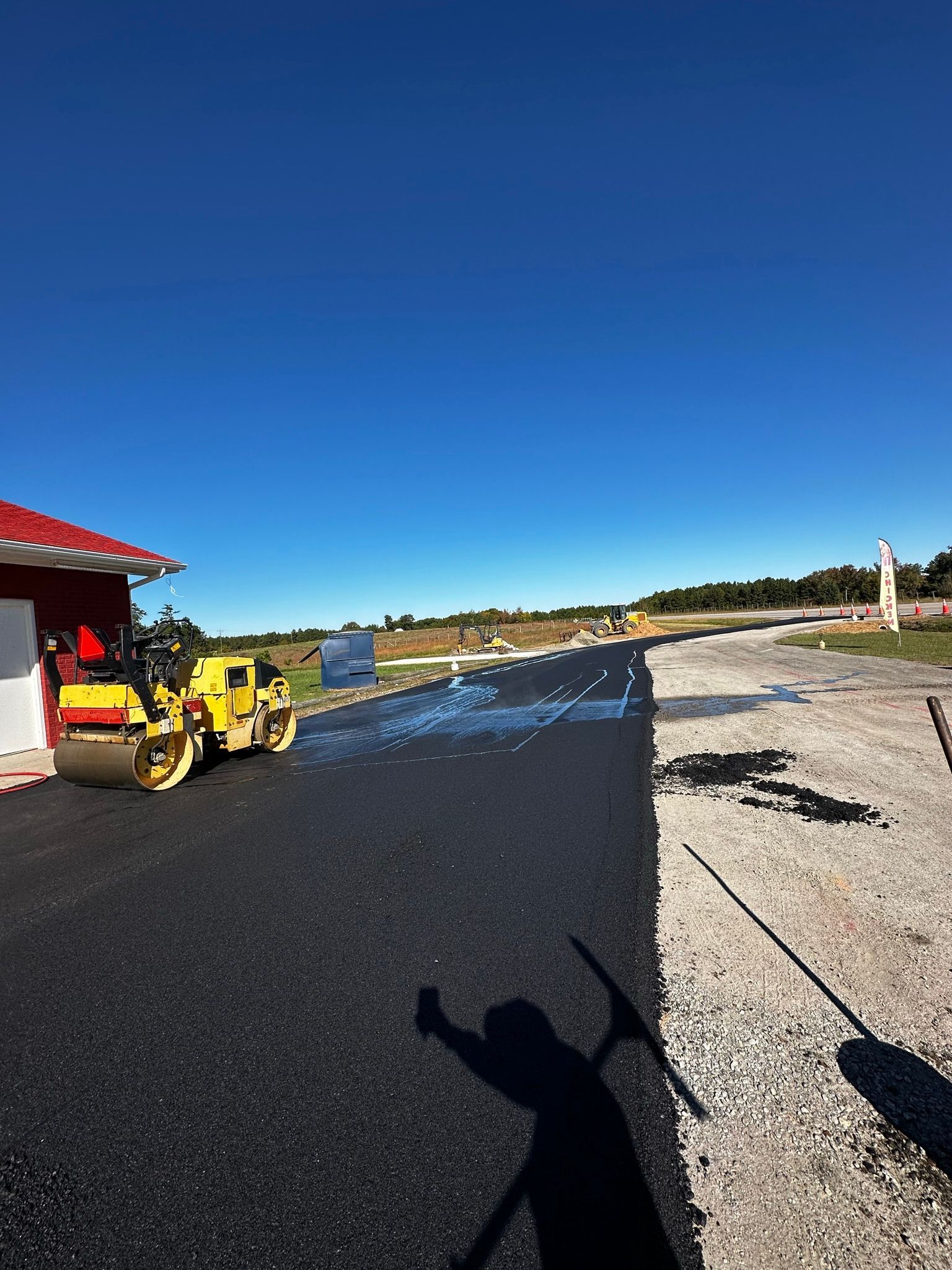 Road paving scene with a yellow roller near a building under a clear blue sky