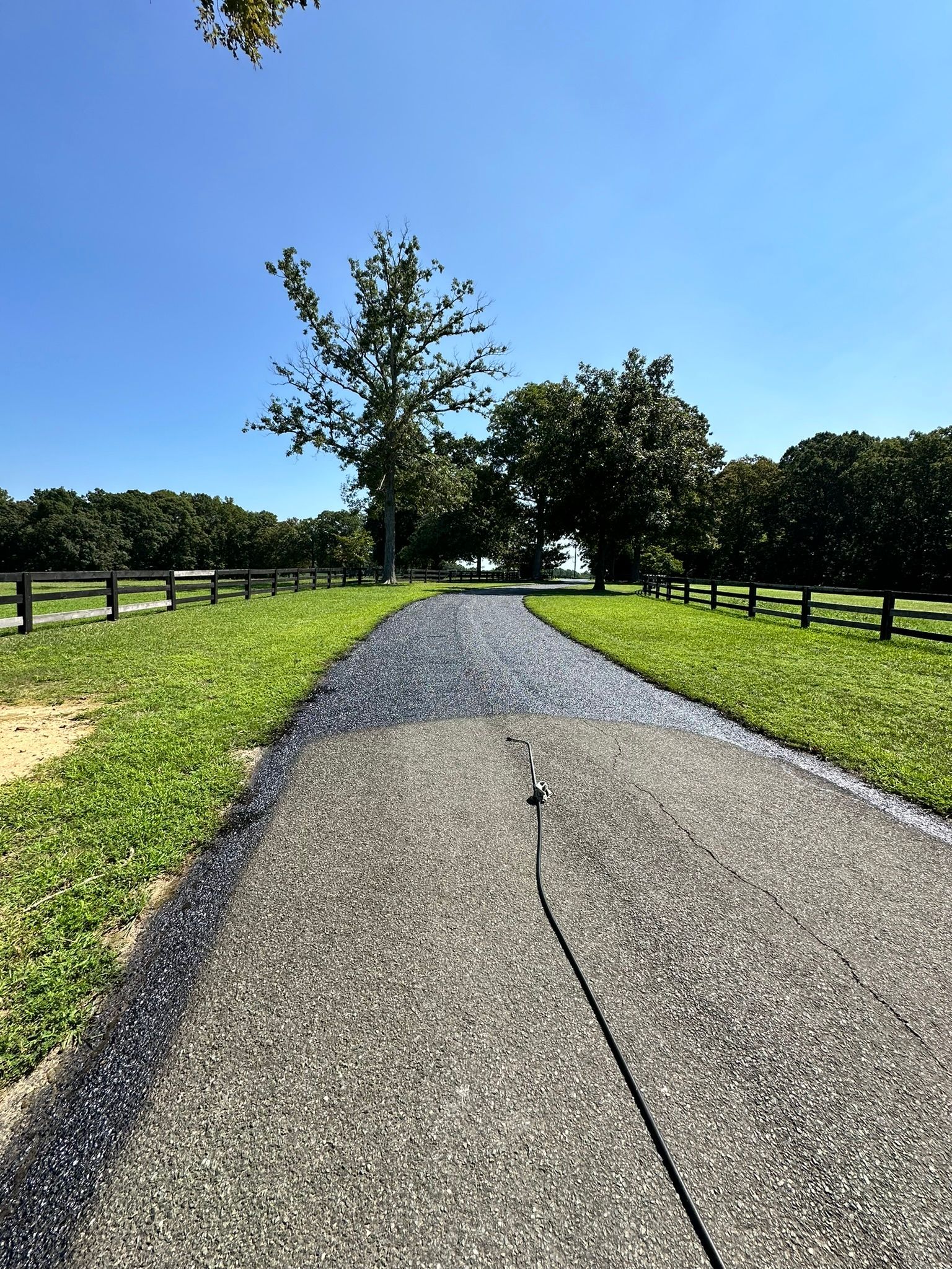 Gravel path through a sunny green park with trees and wooden fences under a blue sky.