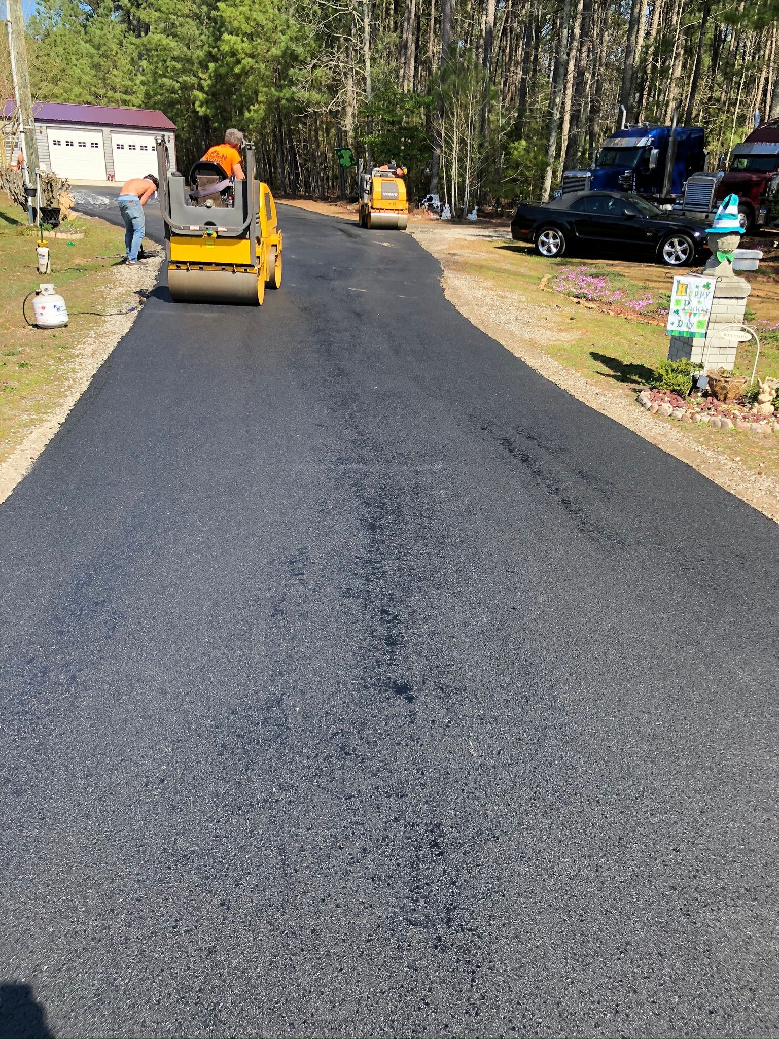 Road paving crew working on a newly laid black asphalt driveway in a wooded area