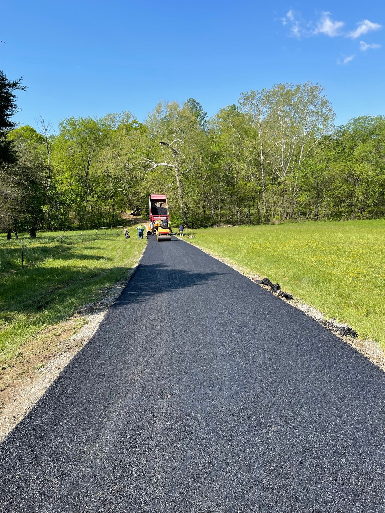 Gravel path leading through a sunny park with trees and a small red cart in the distance