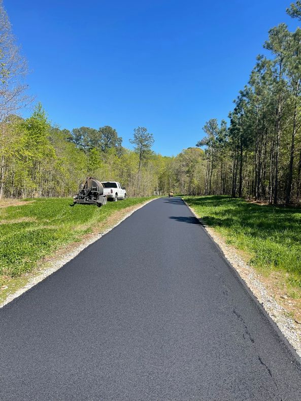 Paved path through trees under a clear blue sky, with a white vehicle parked on the left.