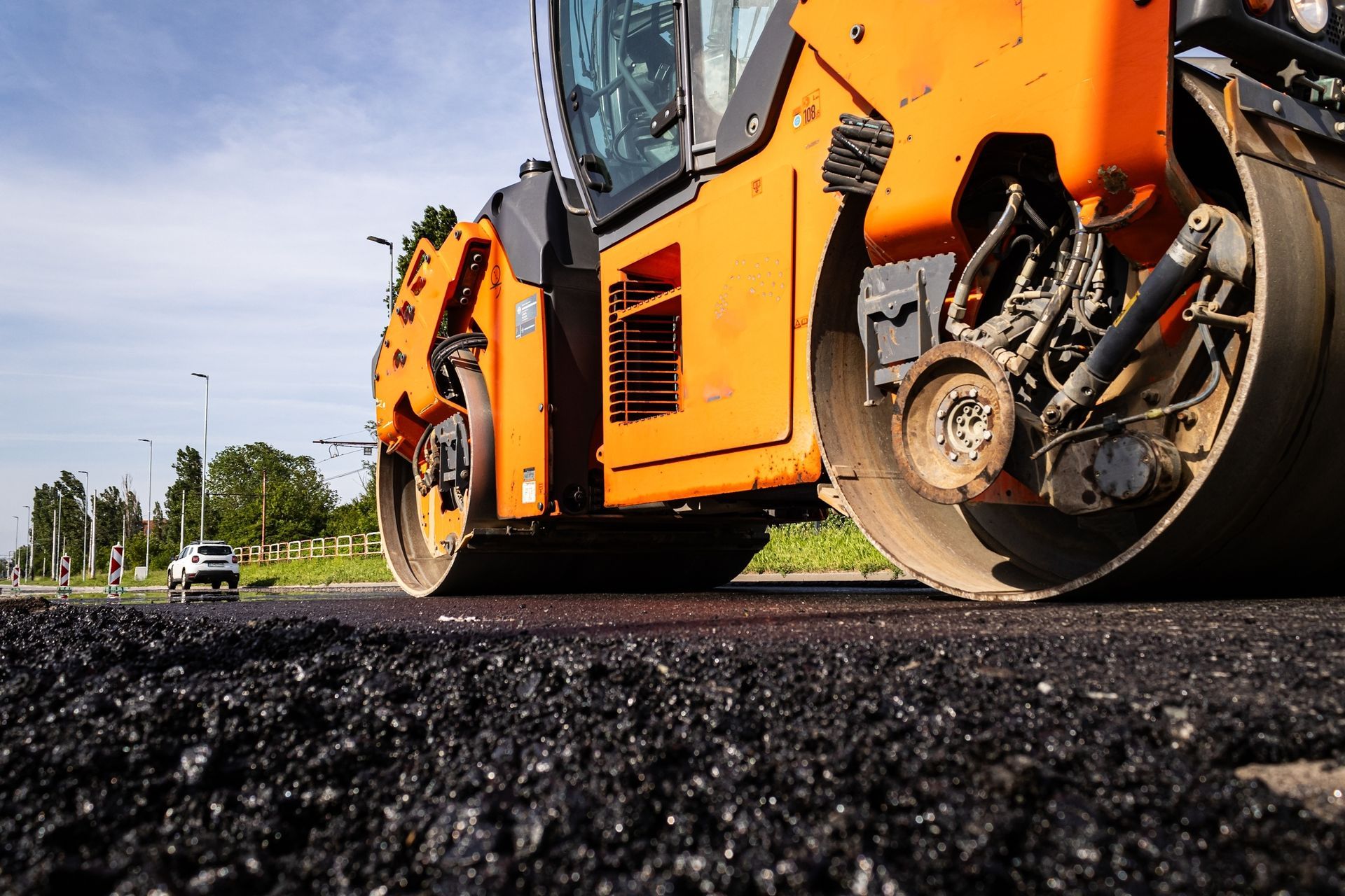 Orange road roller paving black asphalt on a road, low-angle view