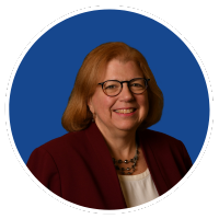 Photo of white woman with reddish brown shoulder length hair, glasses, a red blazer.