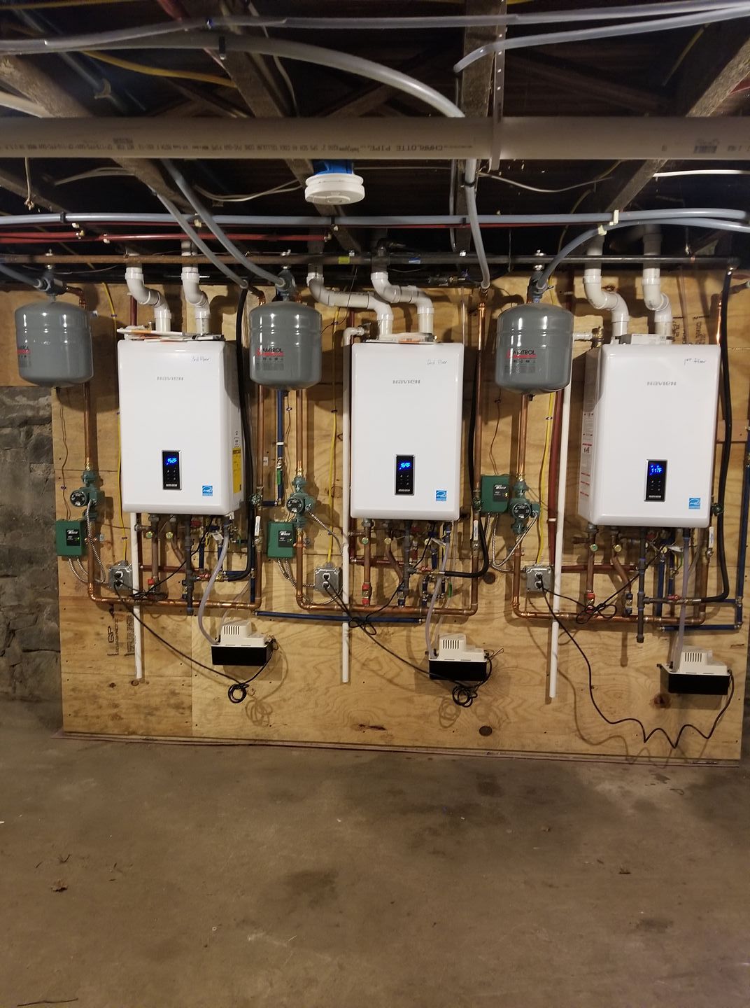 A row of water heaters are lined up on a wall in a basement.