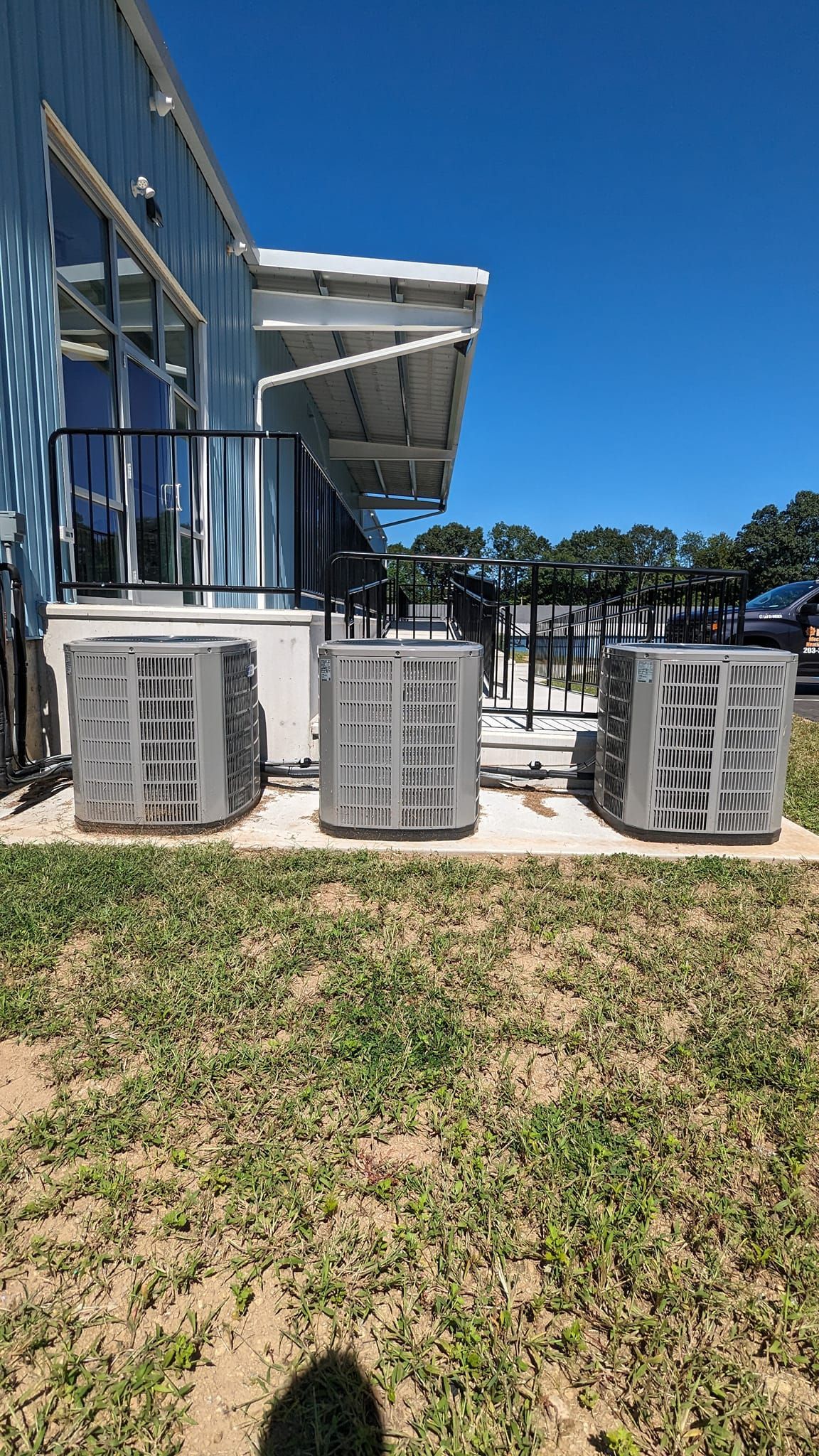 Three air conditioners are sitting in the grass in front of a building.