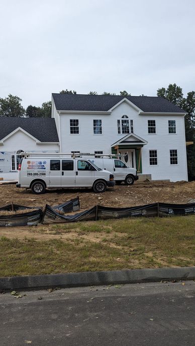 A white van is parked in front of a large white house under construction.