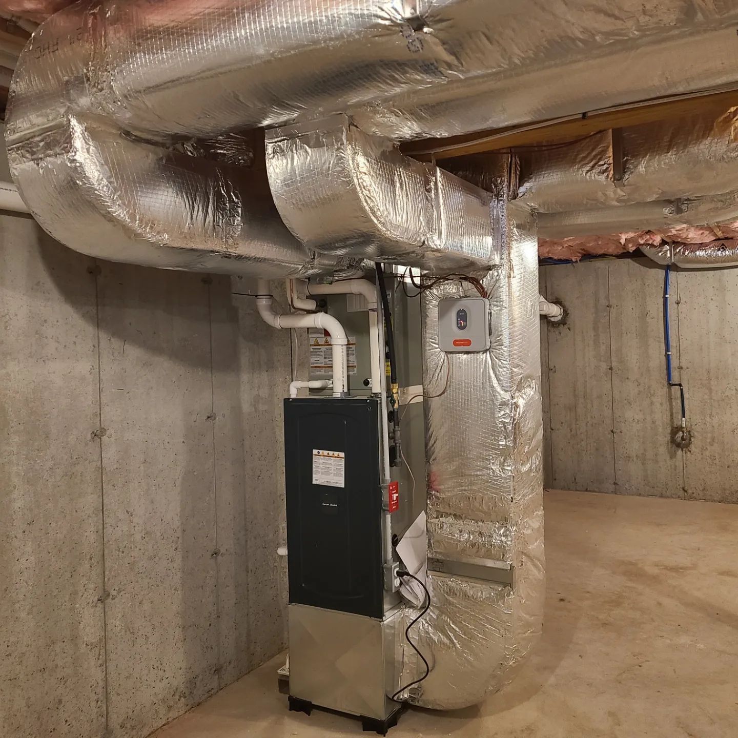 An air conditioner in a basement with a lot of pipes