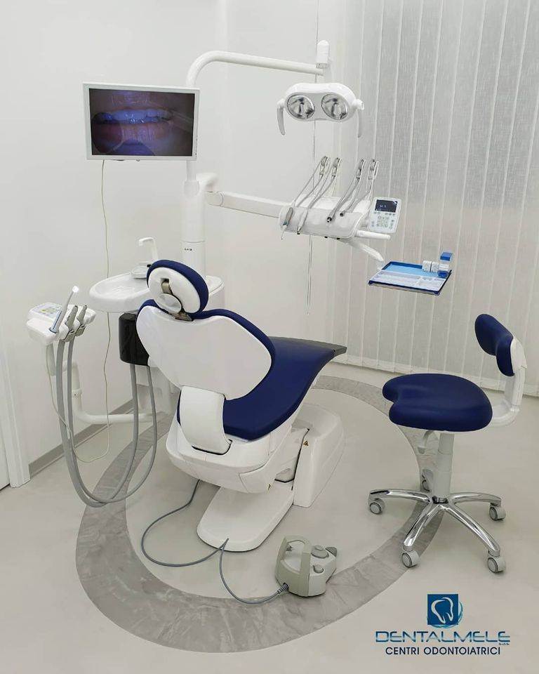 Clinica odontoiatrica moderna con poltrona odontoiatrica bianca e blu, luci a soffitto, monitor e sgabello.