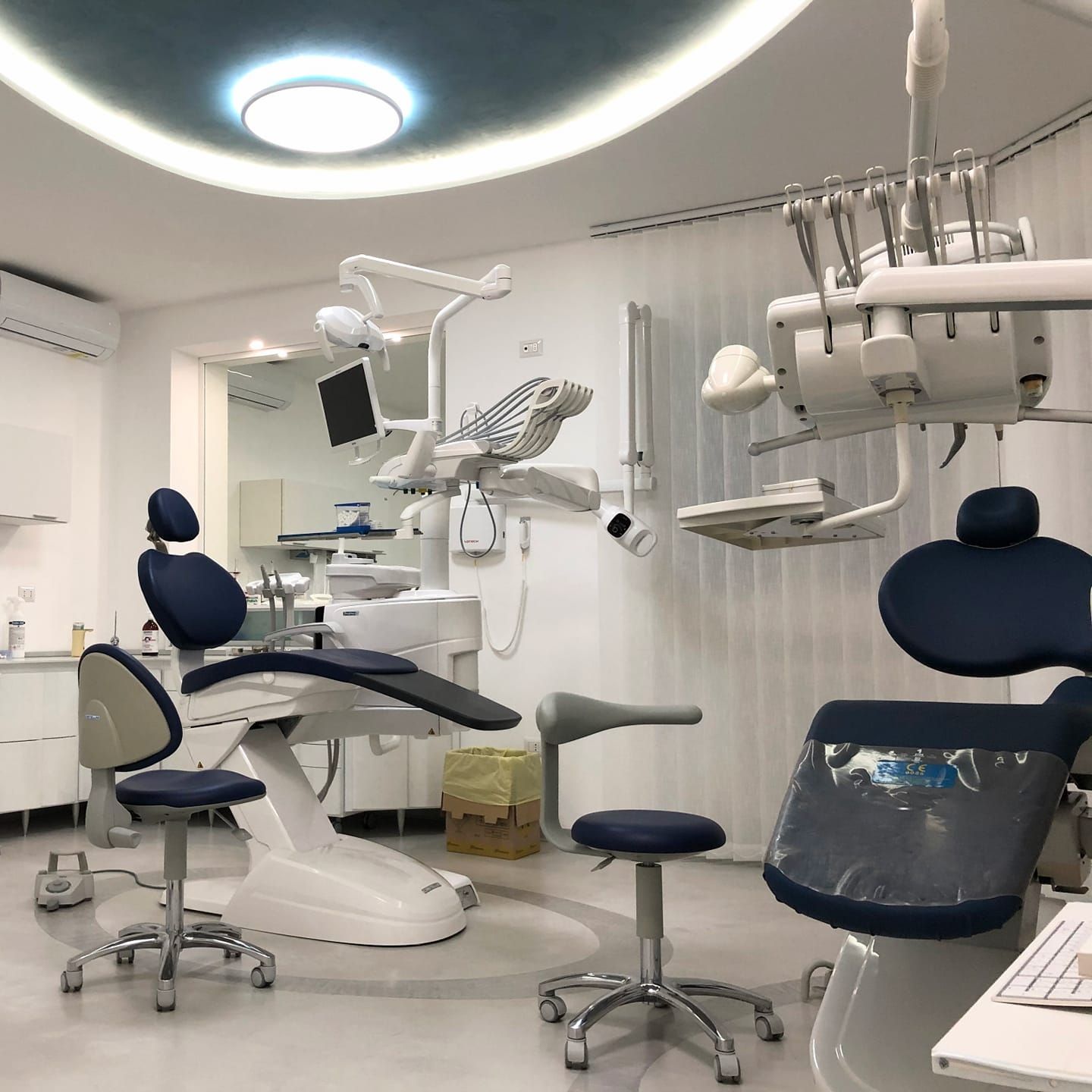 Clinica odontoiatrica moderna con poltrone, luci a soffitto e attrezzature per i trattamenti in una luminosa stanza bianca.