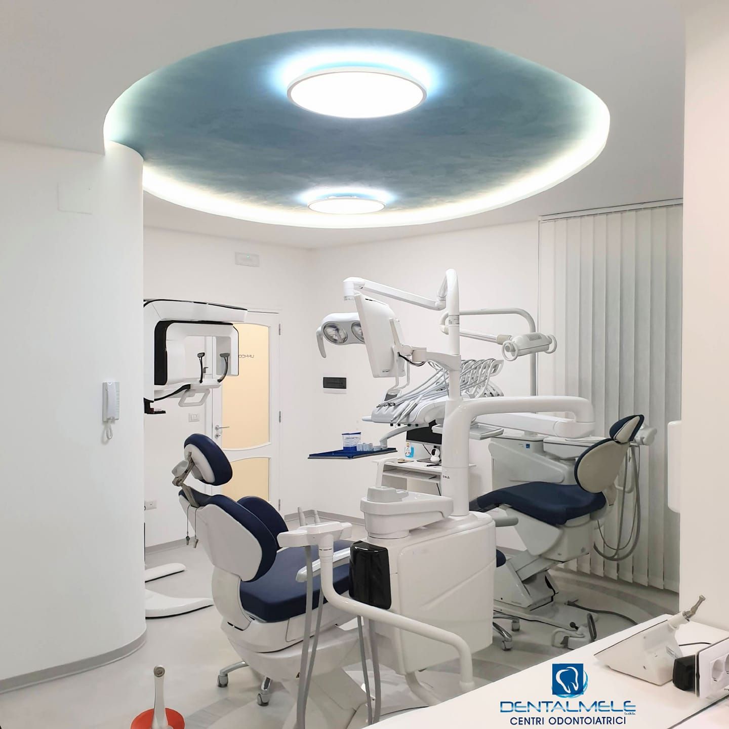 Clinica odontoiatrica moderna con due poltrone, luci a soffitto e attrezzature bianche.