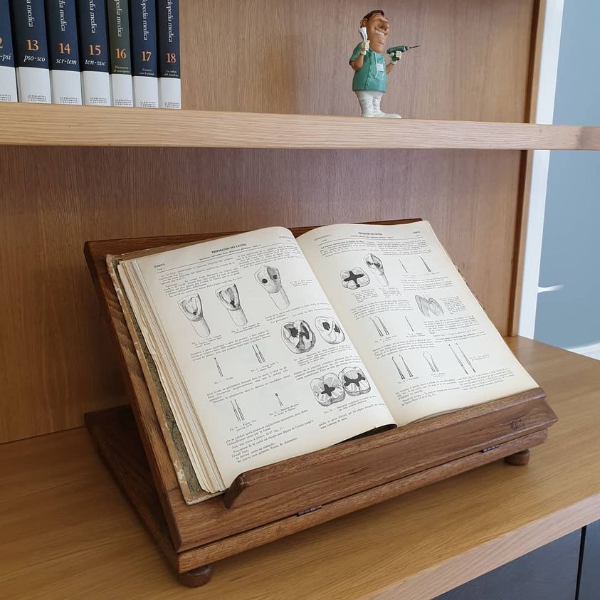 Un libro aperto su un supporto di legno, posto su uno scaffale, con una piccola statuetta sopra di esso.