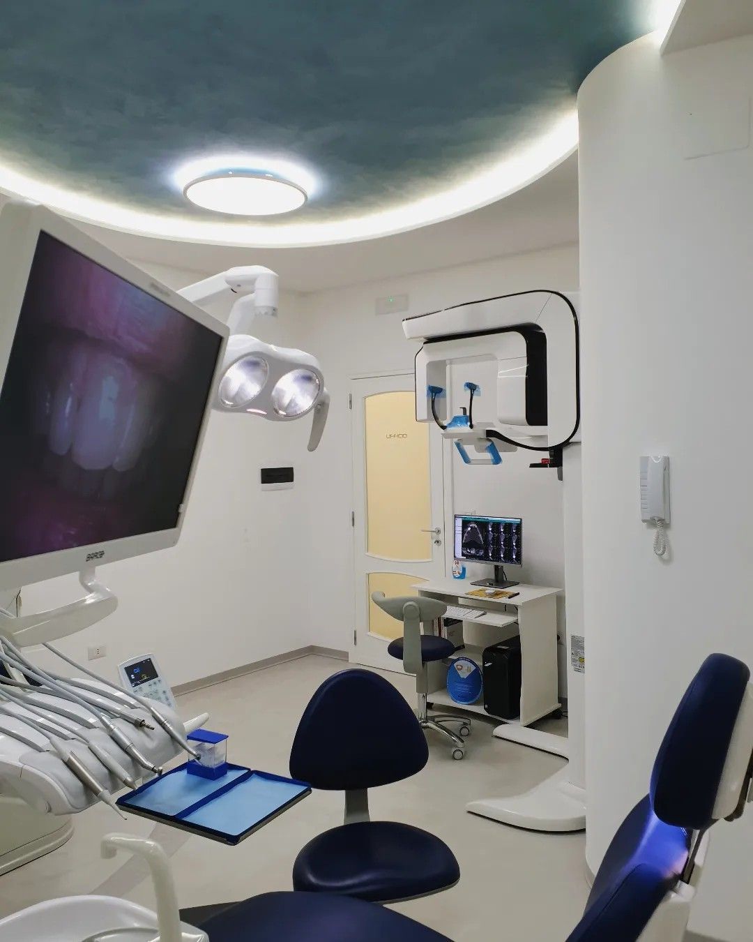 Moderna sala per trattamenti odontoiatrici con poltrona, lampada a soffitto, monitor e attrezzatura.