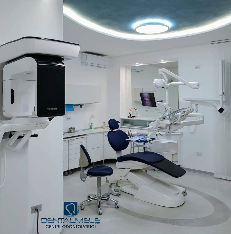 Studio dentistico moderno con apparecchio radiografico, poltrona odontoiatrica e mobili bianchi.