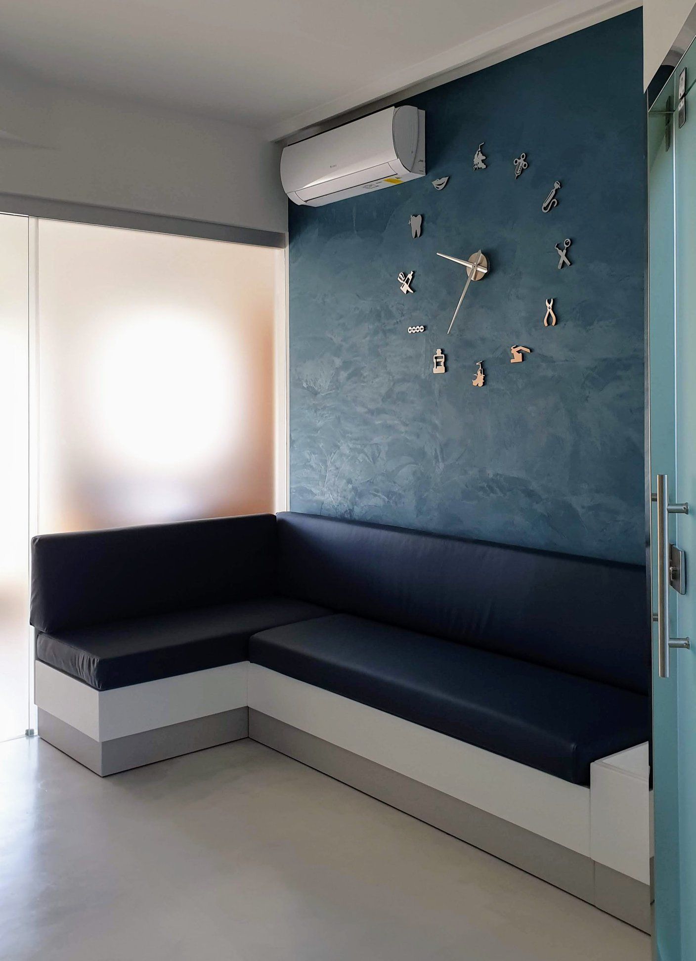 Moderno divano angolare in una stanza luminosa con parete d'accento blu, orologio a parete e condizionatore d'aria.