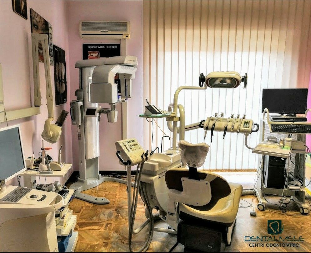Sala odontoiatrica con poltrona, apparecchio radiografico, monitor e strumenti, adiacente a una finestra illuminata dal sole.