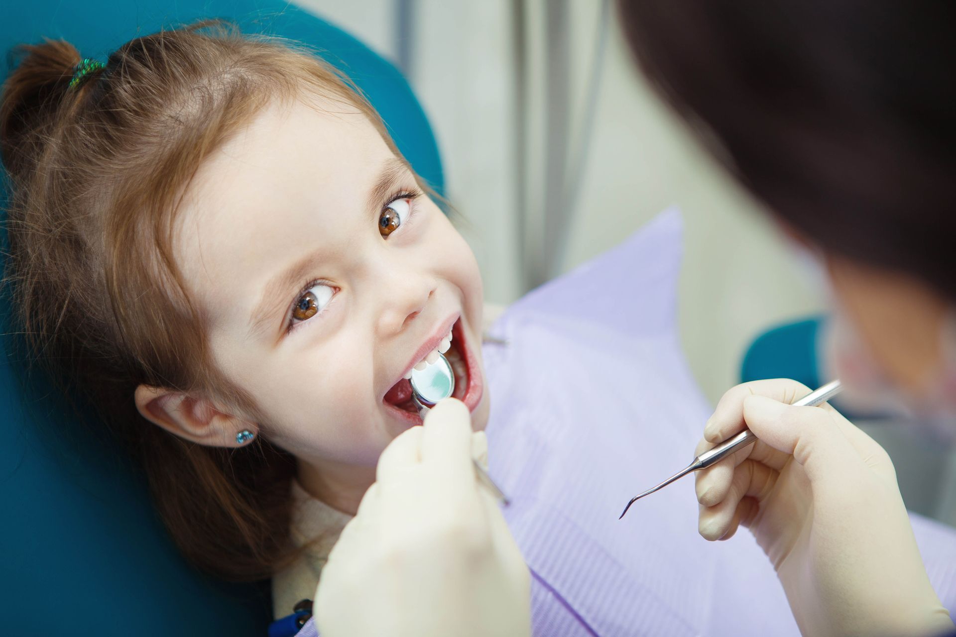 Bambino in visita dal dentista, sorridente mentre il dentista gli controlla i denti con specchietto e strumenti.