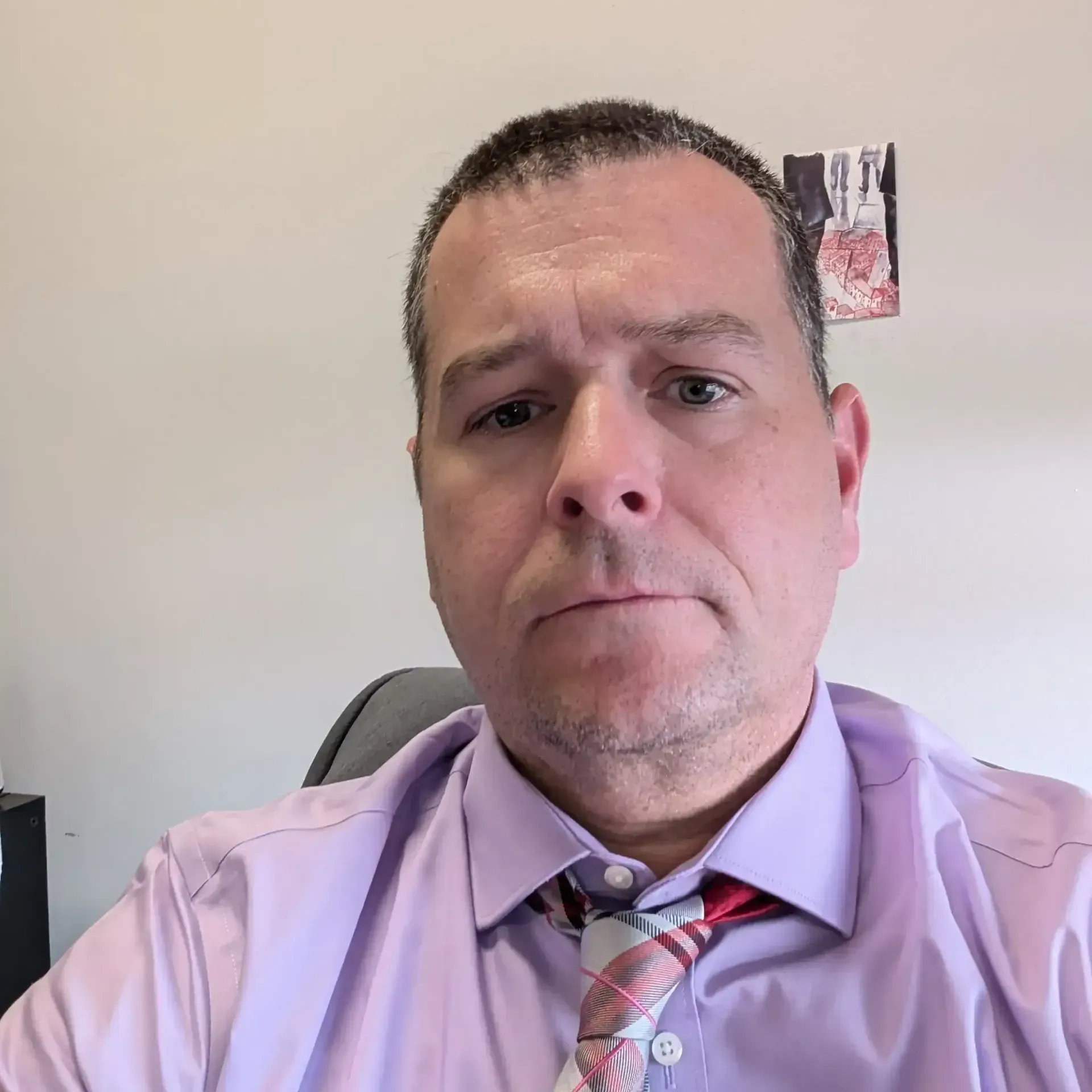 Person in a lavender shirt and patterned tie looking at the camera in an office.