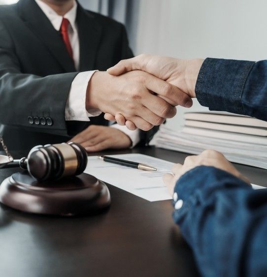 Handshake between two people across a desk, with a gavel and stacks of documents in a legal office.