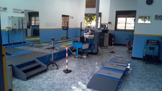 Interno di un'officina con macchinari e un grande rimorchio per camion in riparazione. Gru e attrezzature gialle.