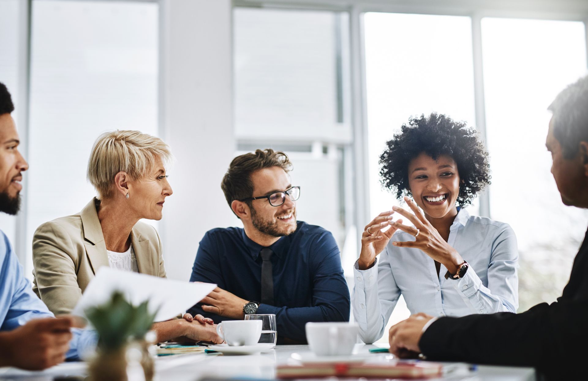 People at a meeting, smiling and discussing; white room, light coming through windows. People at a meeting, smiling and discussing; white room, light coming through windows.