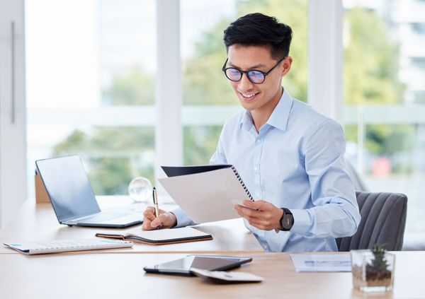 Man wearing glasses smiles while reviewing documents at a desk in an office. Man wearing glasses smiles while reviewing documents at a desk in an office.