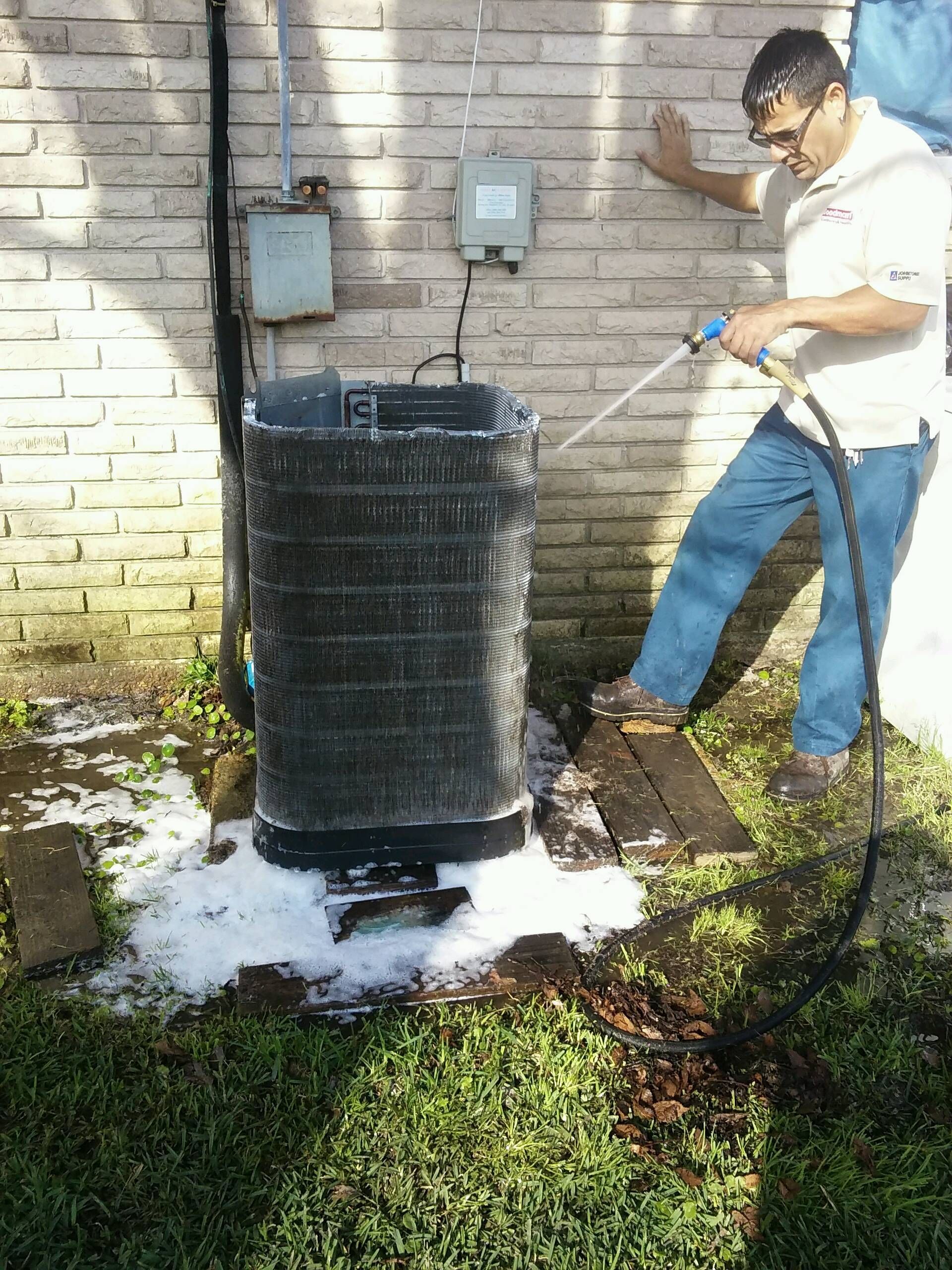 A man is cleaning an air conditioner with a hose.