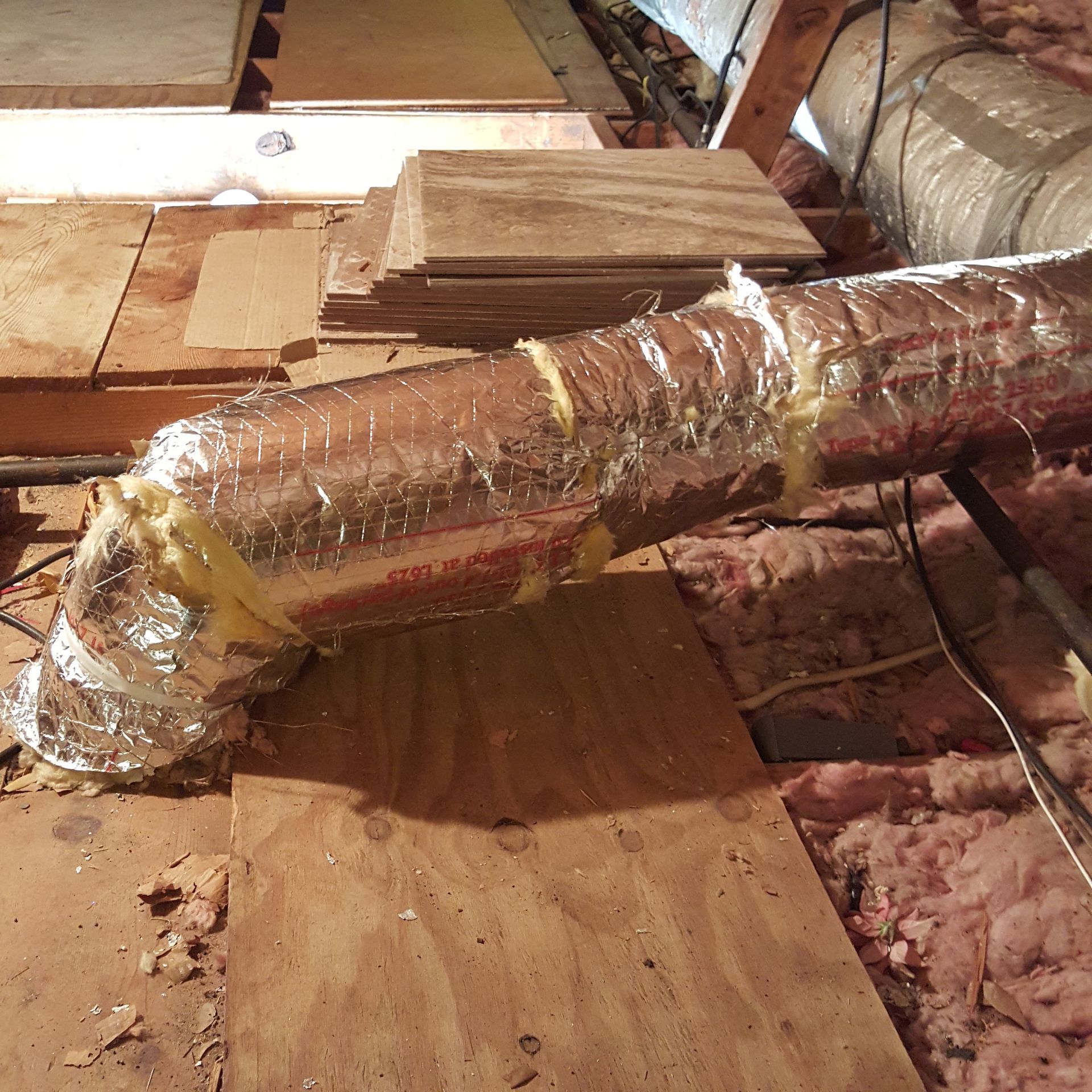 A duct with aluminum foil wrapped around it is sitting on a wooden floor