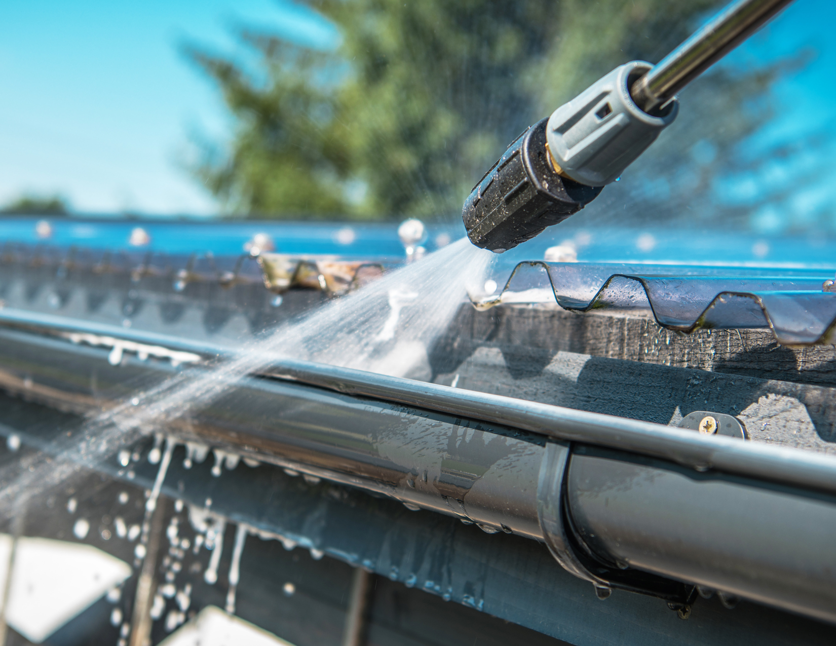 A person is cleaning a gutter with a high pressure washer.