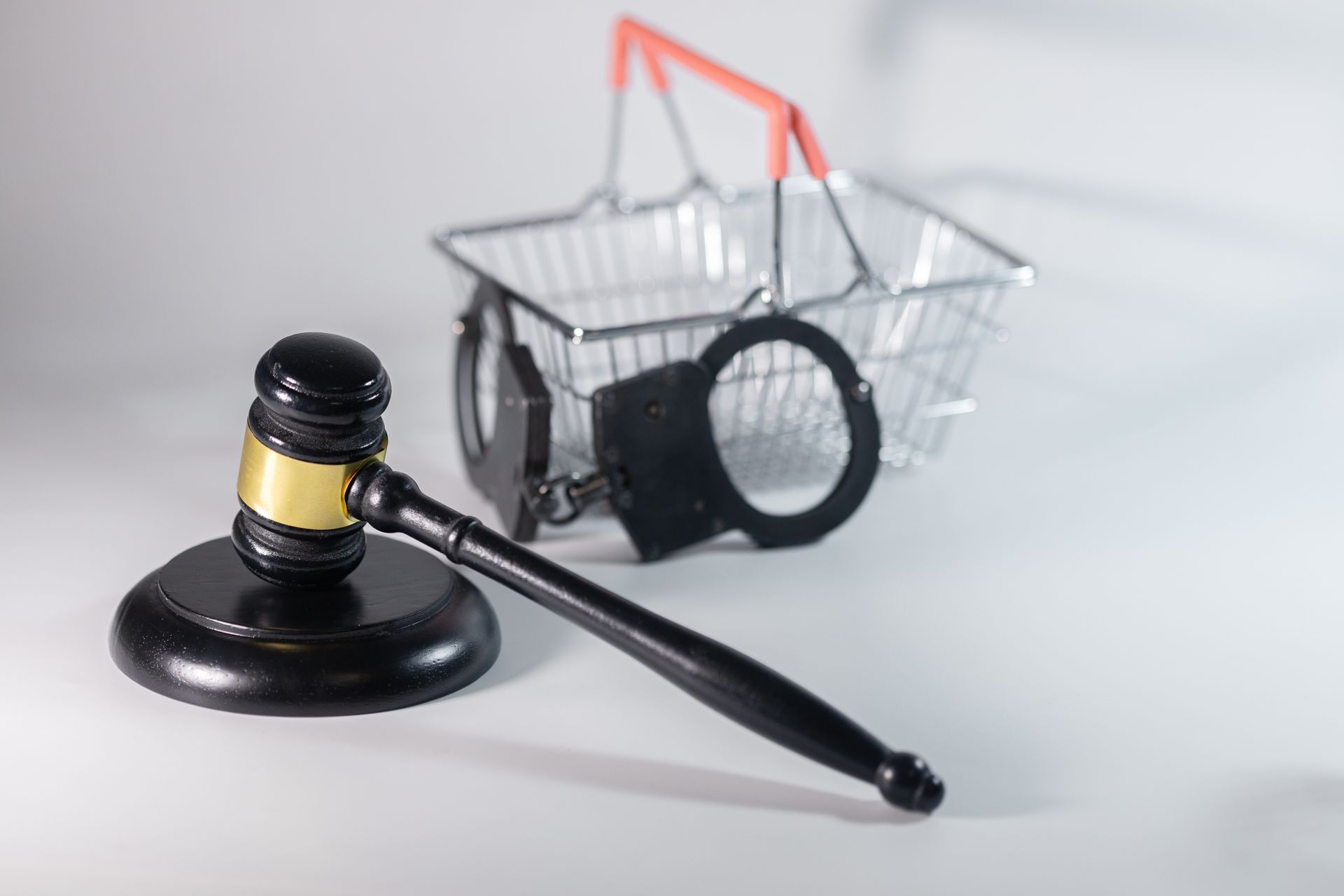 A hand holds a pair of handcuffs, next to a wooden gavel, in front of a white background. A hand holds a pair of handcuffs, next to a wooden gavel, in front of a white background.