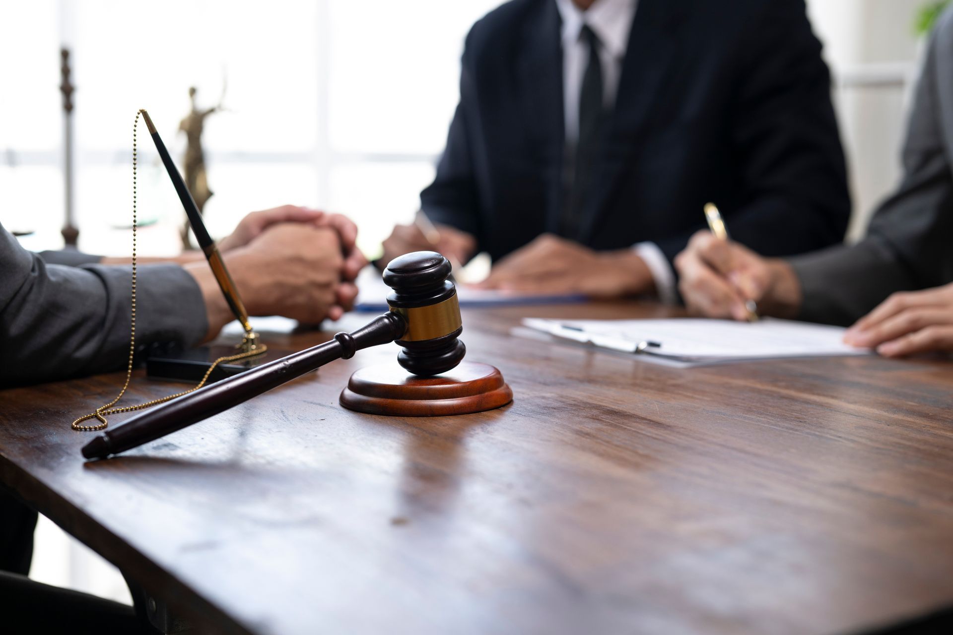 Lawyers discuss and sign a legal contract at a table with a judge's gavel nearby.