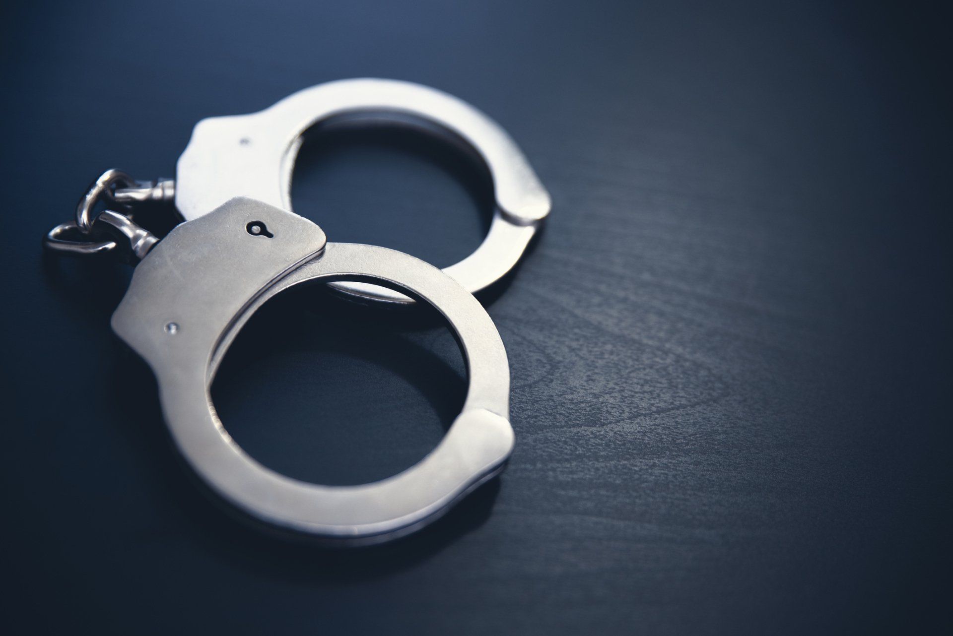Silver handcuffs on a dark blue surface.