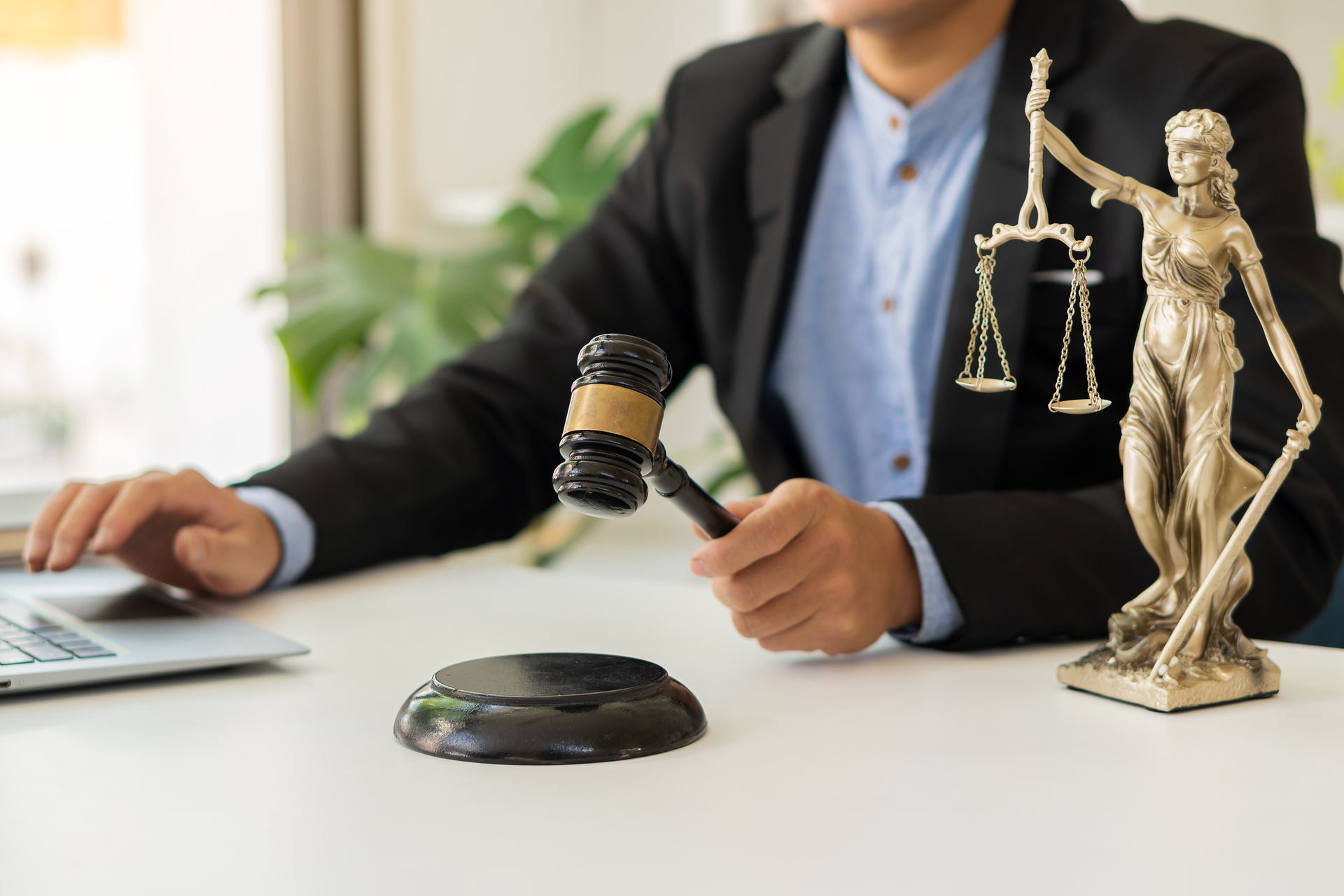 Judge with gavel and laptop, Lady Justice statue in foreground.