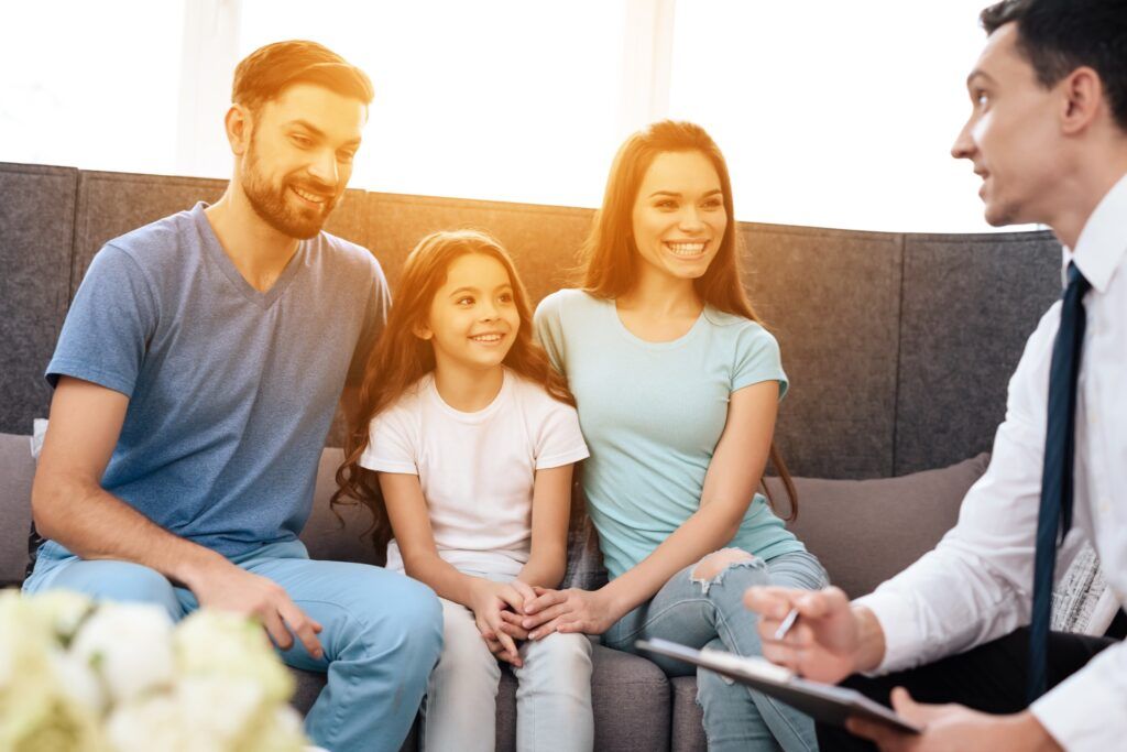 a family is sitting on a couch talking to a man .