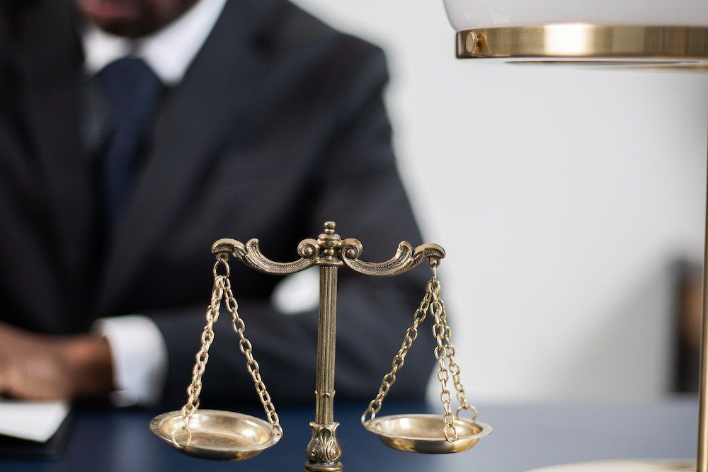 a man in a suit and tie is sitting at a table with a scale of justice in front of him .