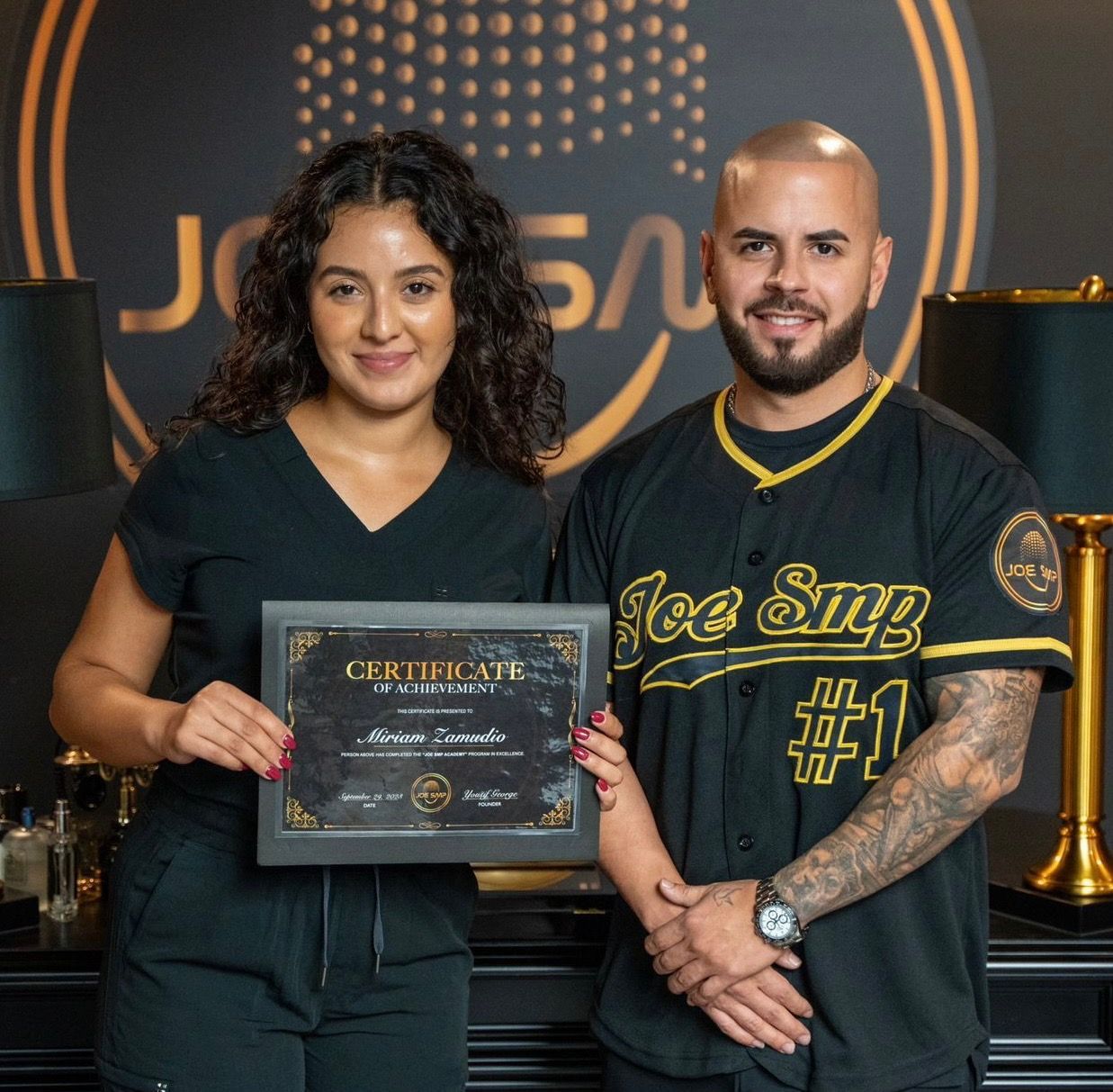 Woman and man holding certificate; Joe Sup logo in background. They are smiling.