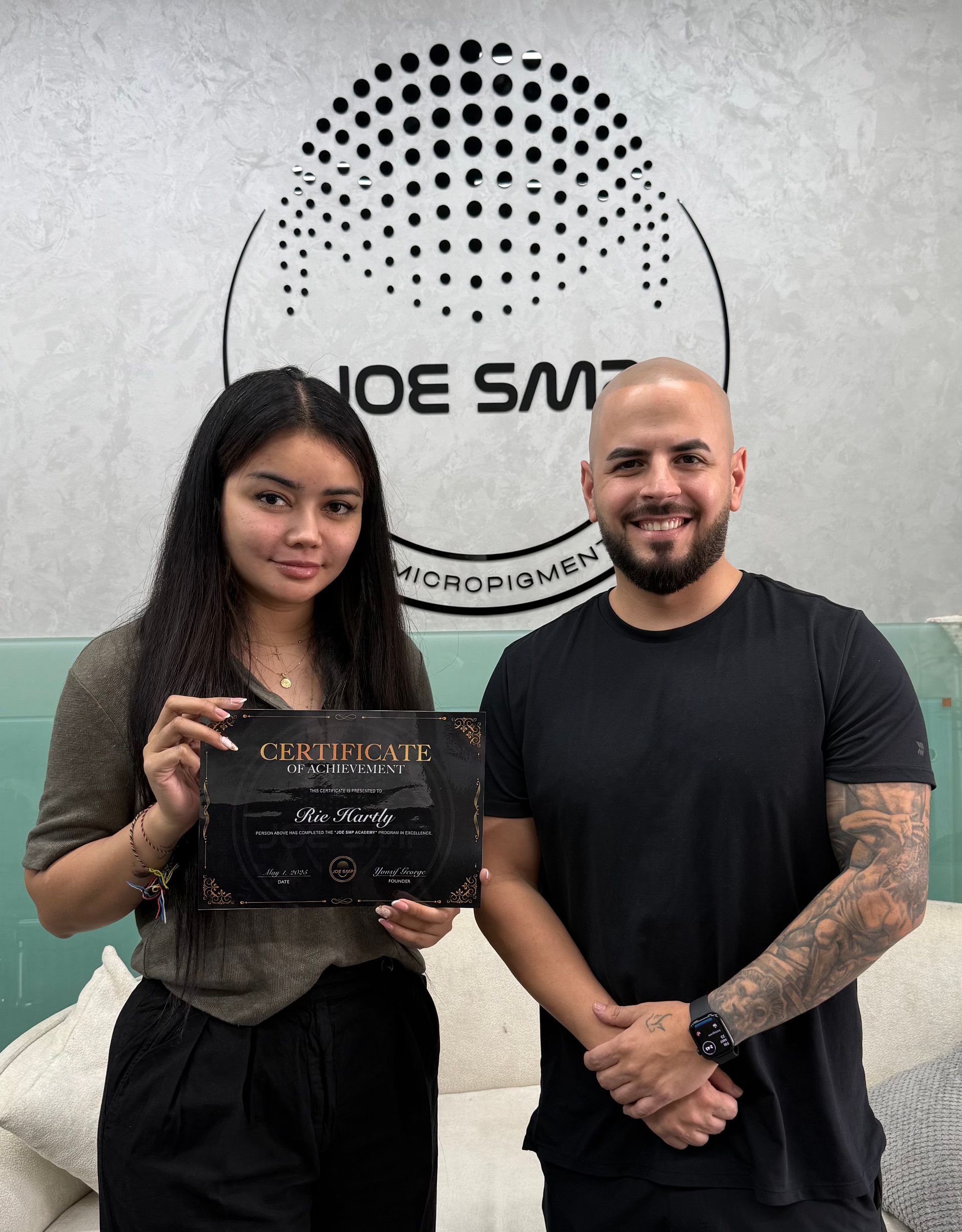 Woman and man holding certificate in front of a logo. They are smiling. Modern office setting.