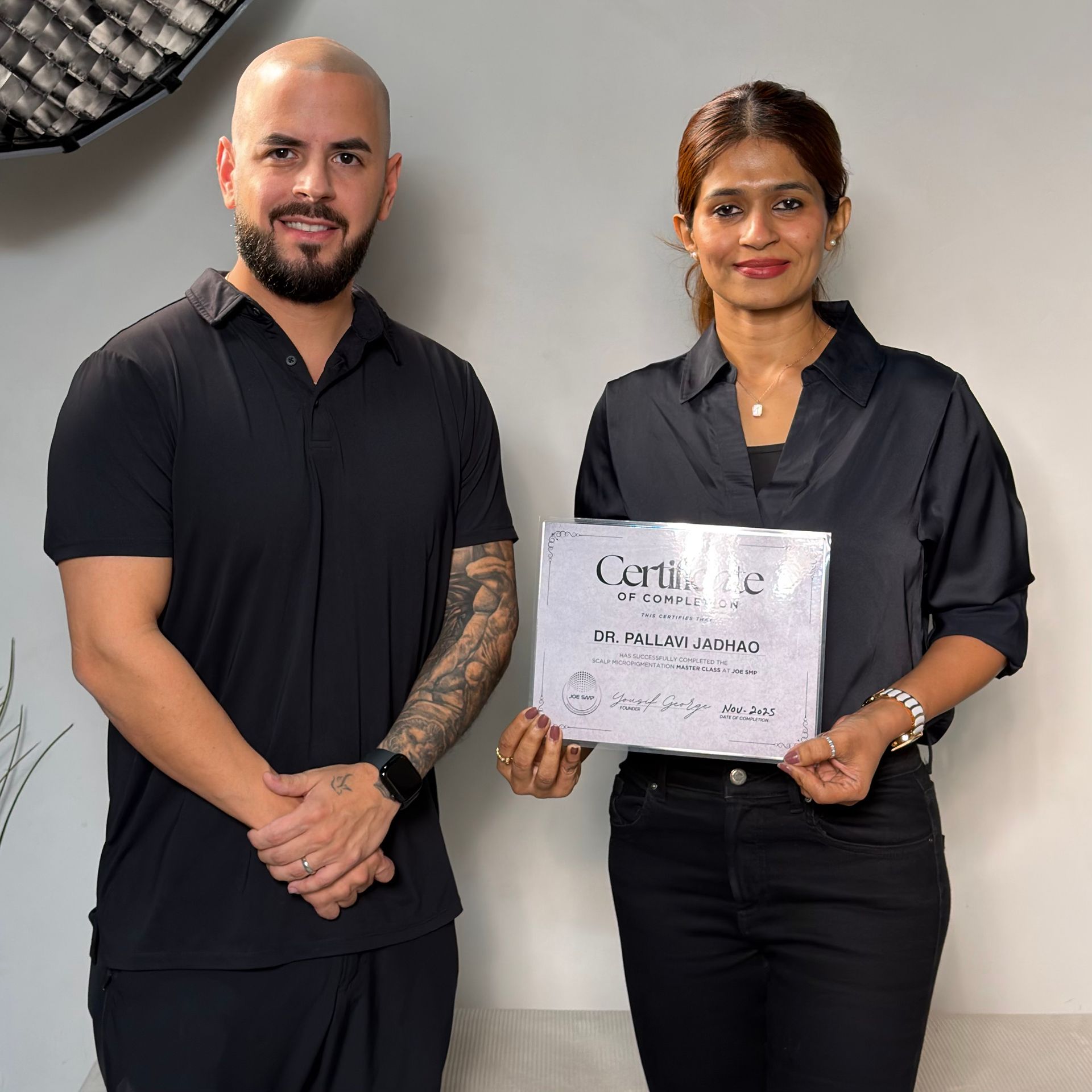 Two people holding a certificate, both dressed in black. Indoors. Smiling.
