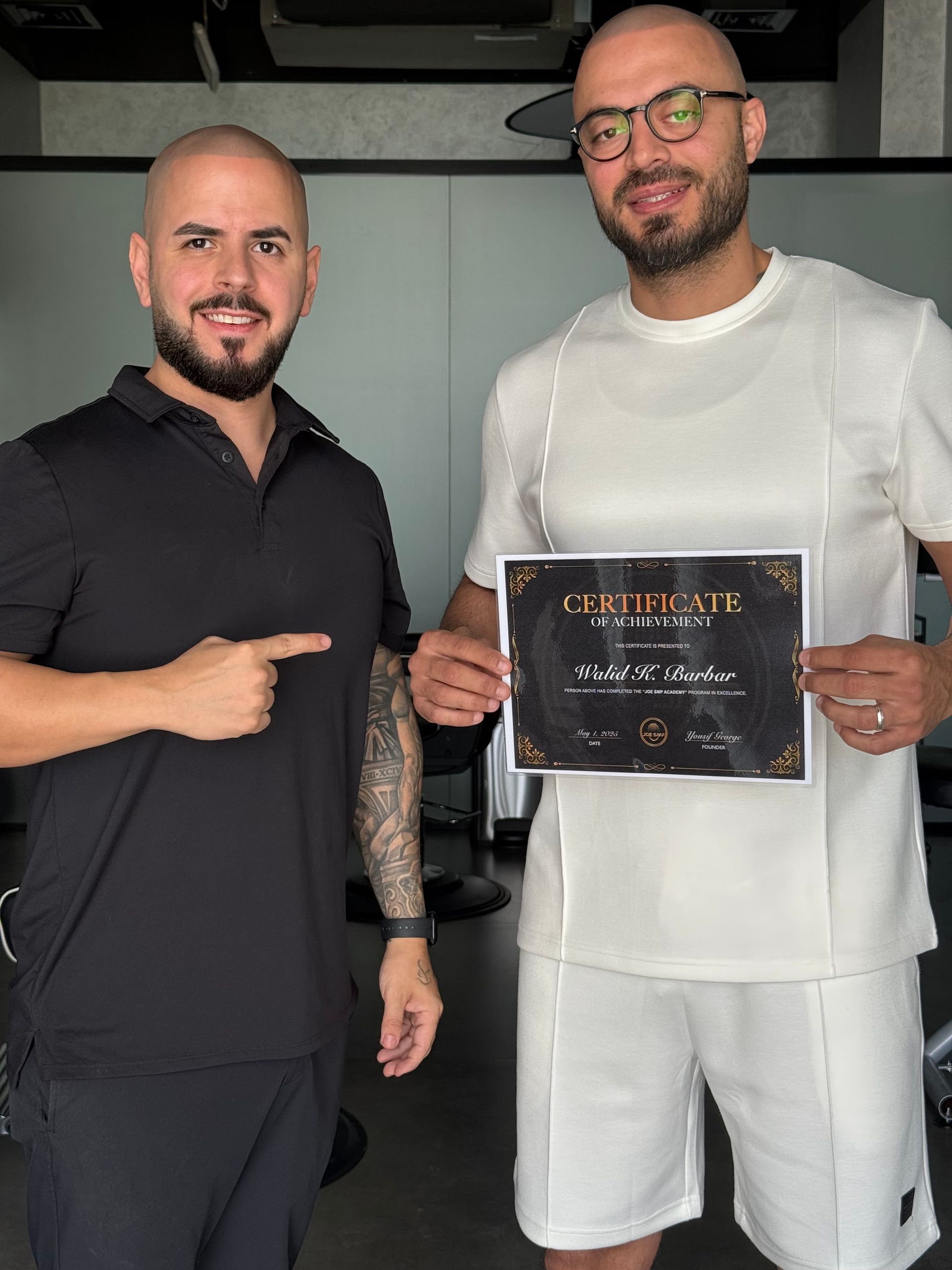 Two men holding a certificate; one points, smiling. Setting is indoors.