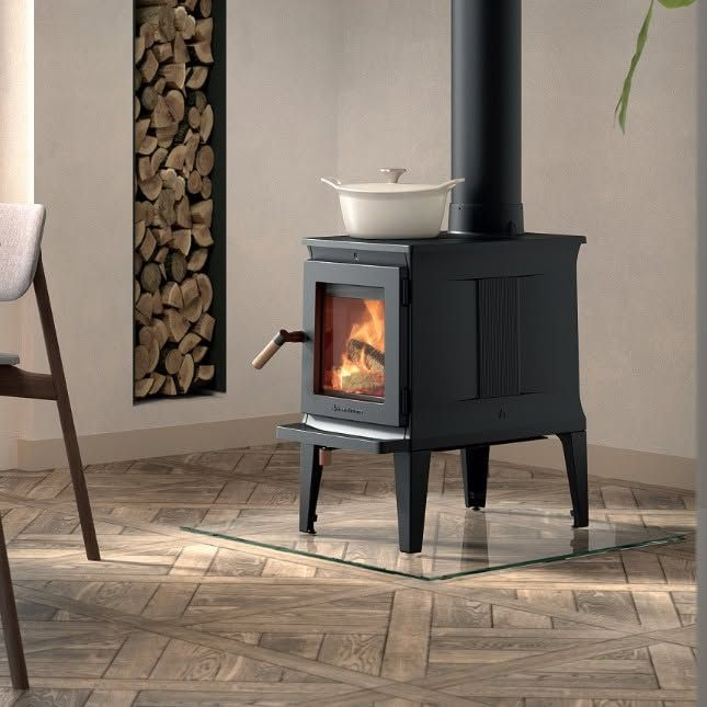 A black wood-burning stove with a fire burning inside. It has ornate details, a curved glass door, and is set against a white background.